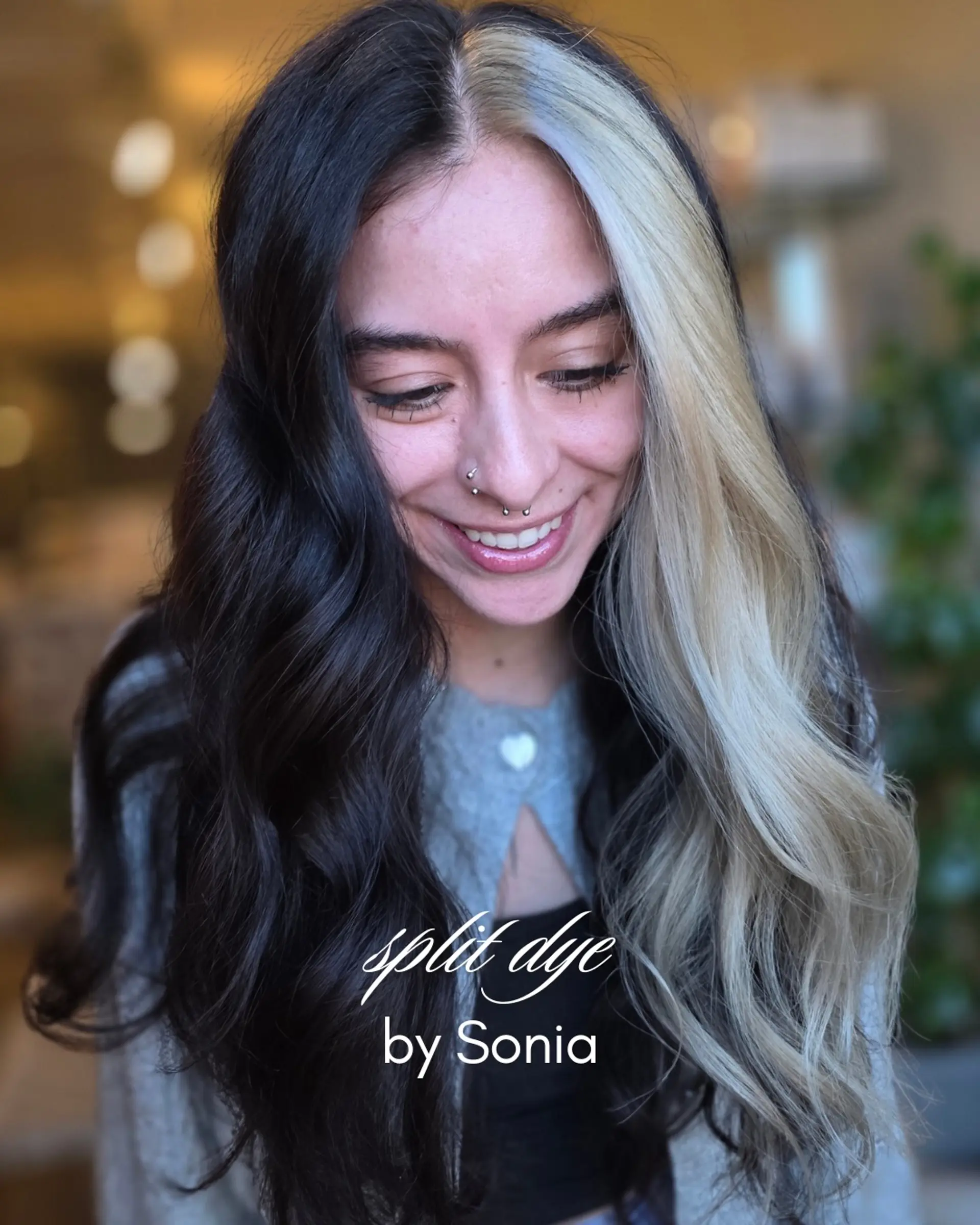 A bold split dye style featuring jet black hair on one side and cool platinum blonde on the other with a clean center part and soft waves. 1
