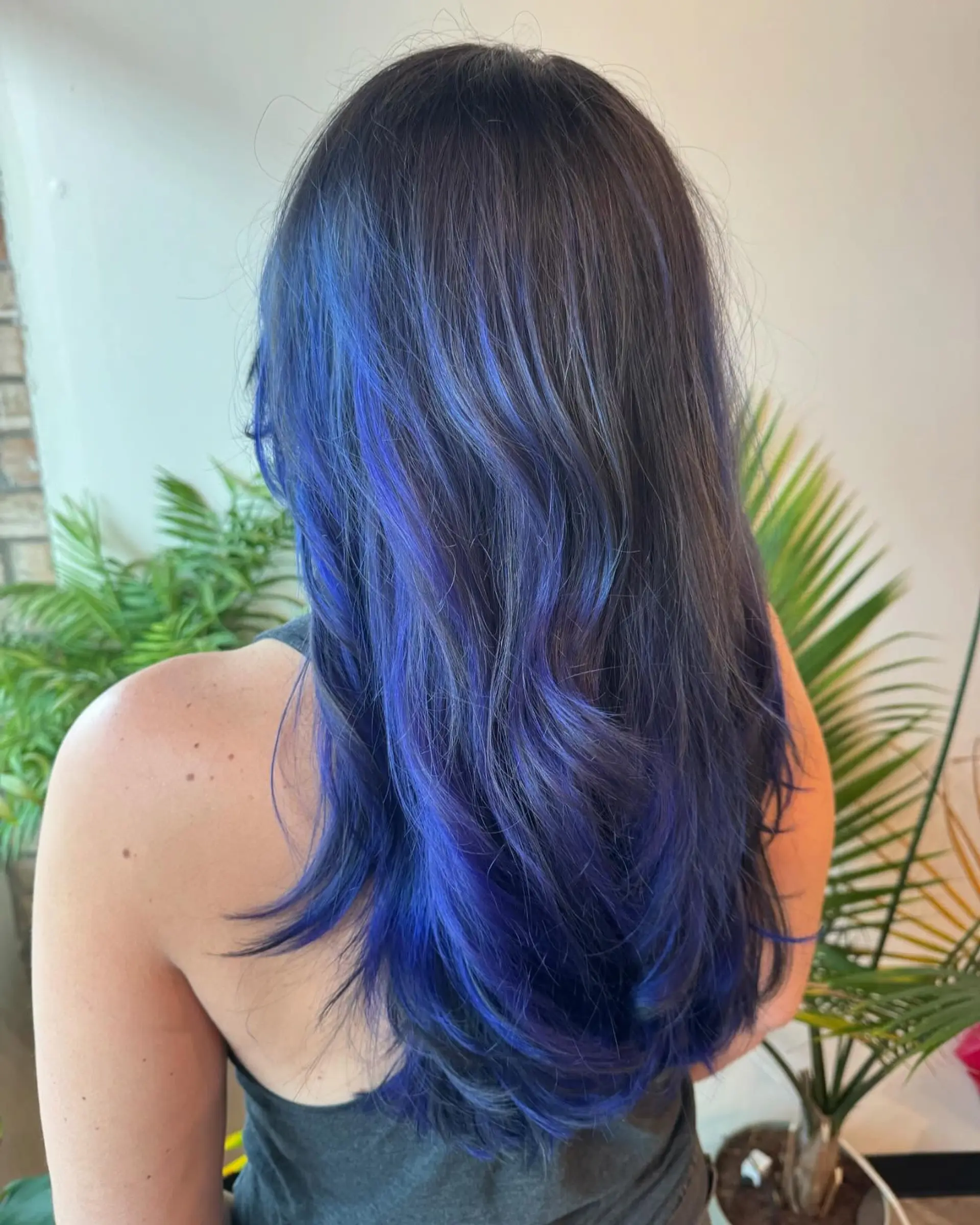 Long layered dark hair infused with vibrant electric and cobalt blue balayage highlights styled in soft waves. 1