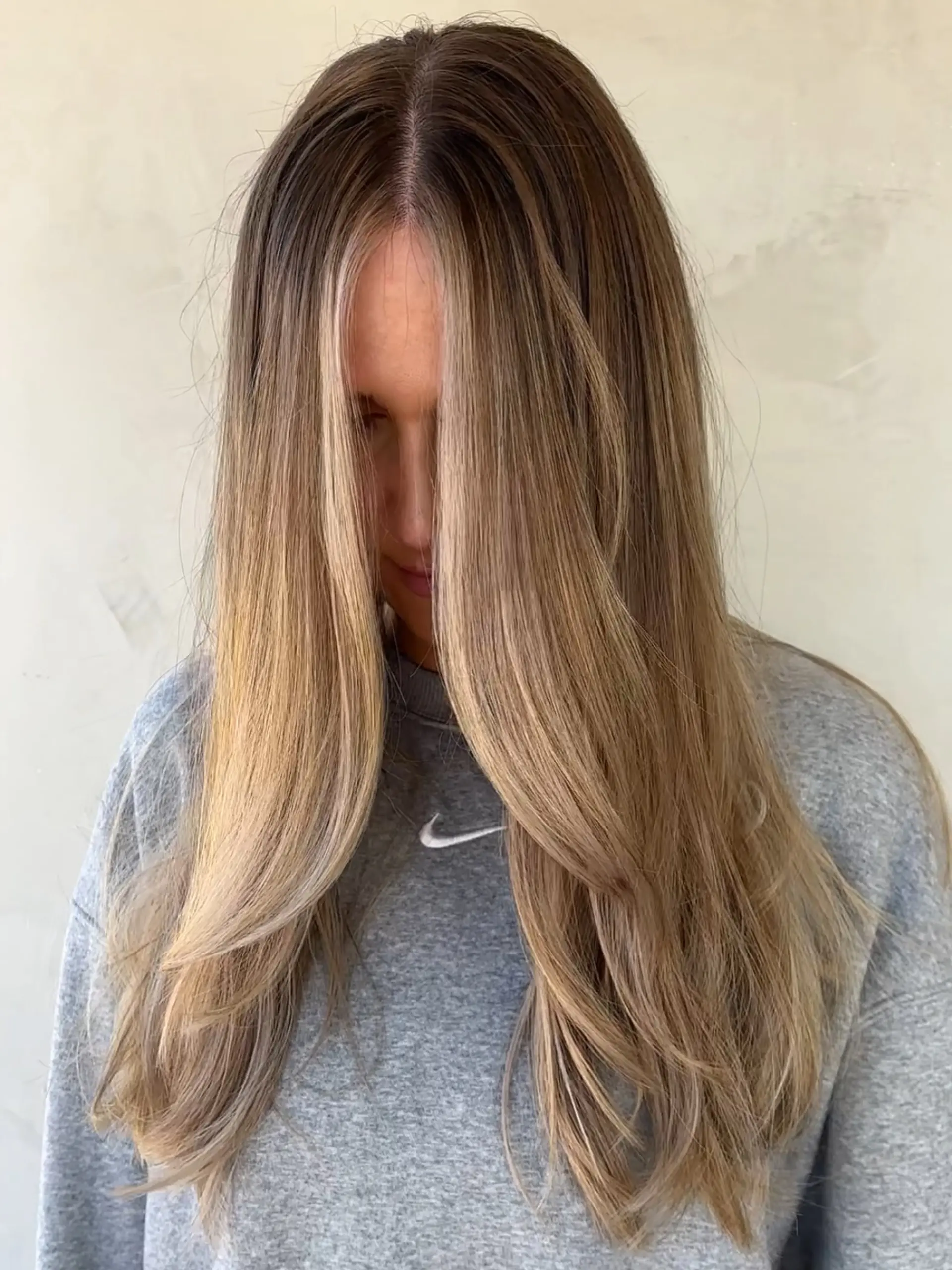 Long layered hair styled straight with gentle bevels at the ends, featuring bright blonde balayage highlights seamlessly blended from a natural root. 1