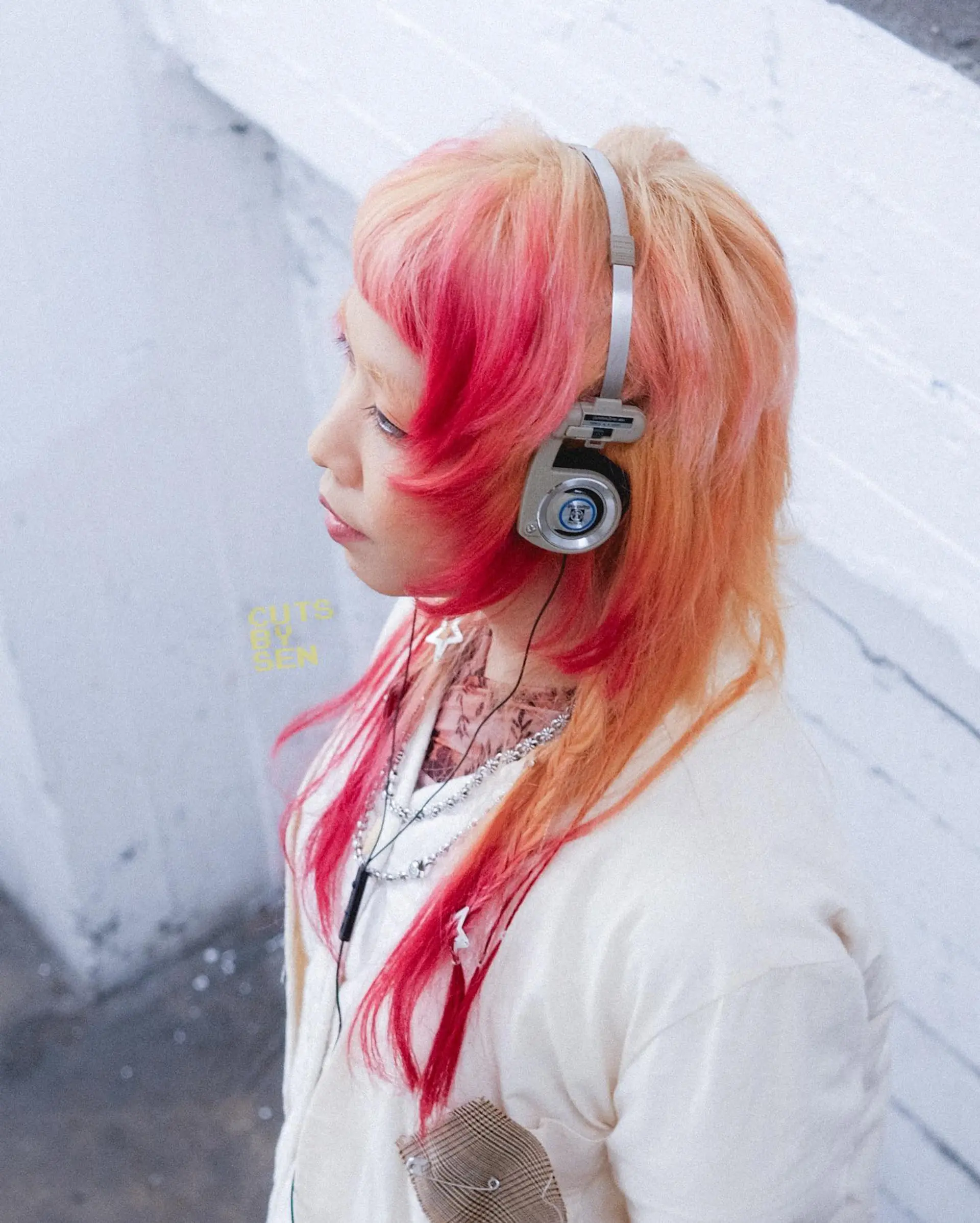 An edgy, layered hime cut featuring textured bangs, cheek-framing steps, and vibrant streaks of magenta pink blended into a peachy blonde base. 1