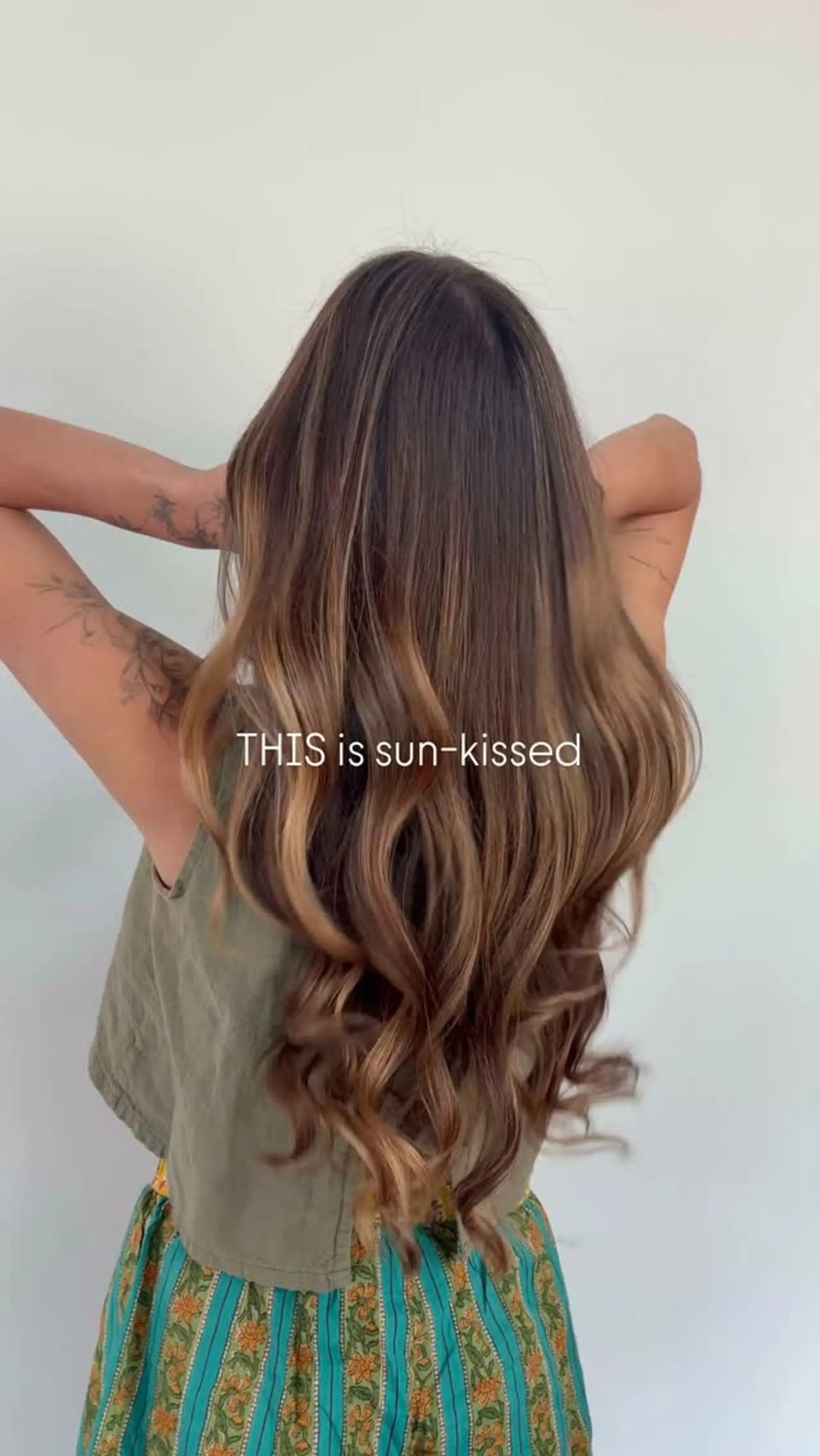 Long wavy brunette hair highlighted with a sun-kissed caramel foilayage that blends seamlessly from roots to ends. 1
