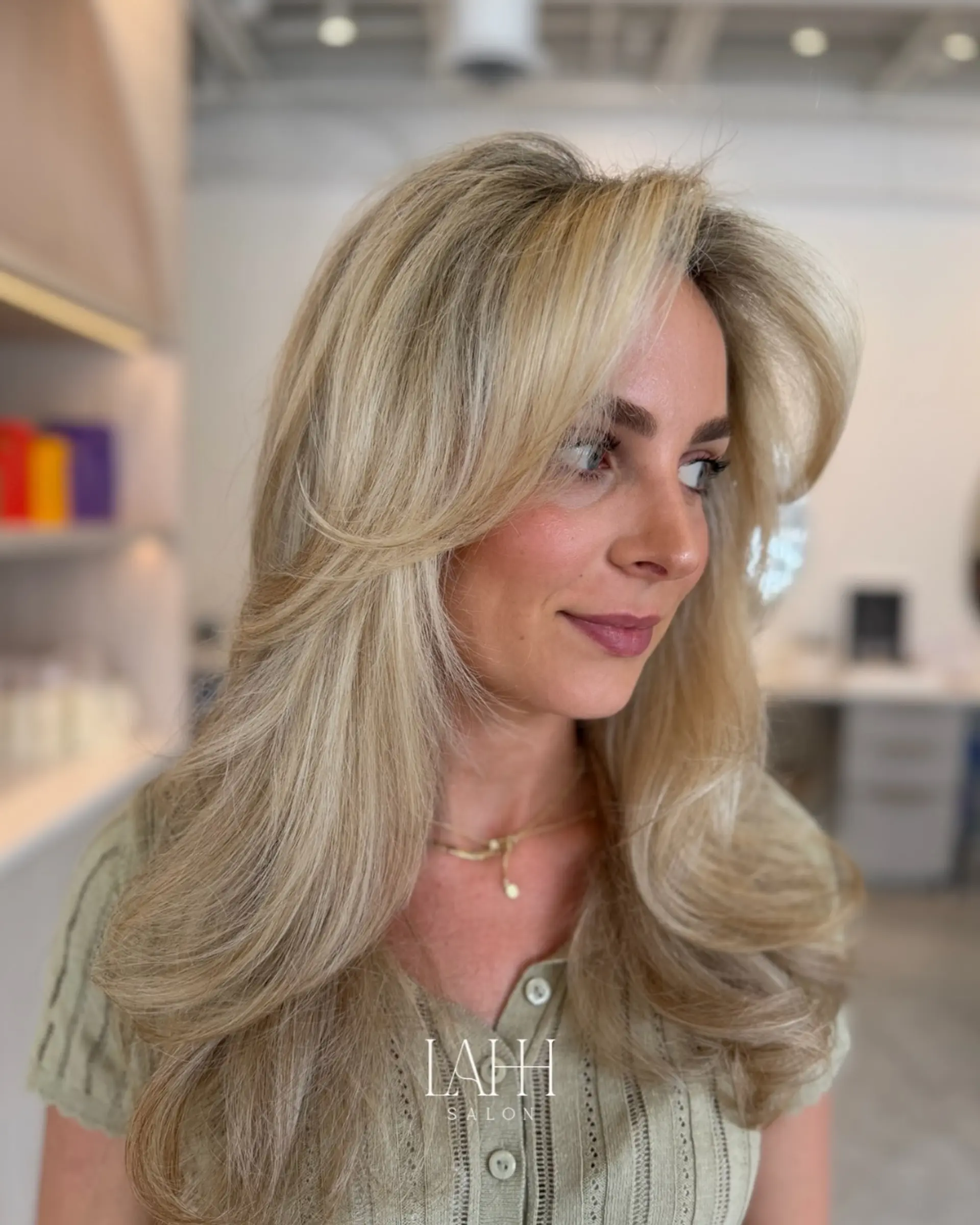 A glamorous long blonde hairstyle cut with soft face-framing layers and styled into a voluminous, bouncy blowout. 1