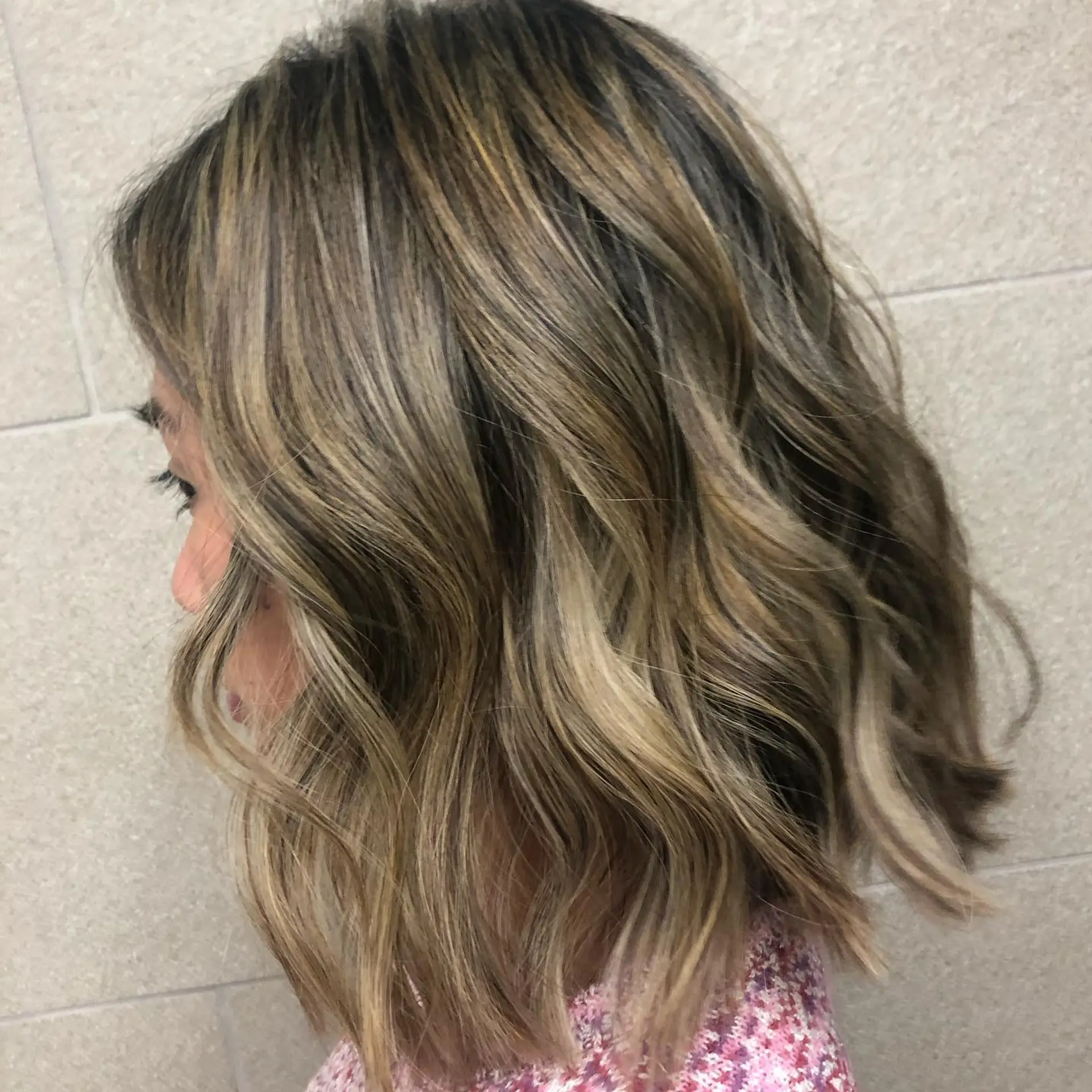 A shoulder-length lob featuring dimensional blonde highlights and balayage styled into relaxed, textured beach waves. 1