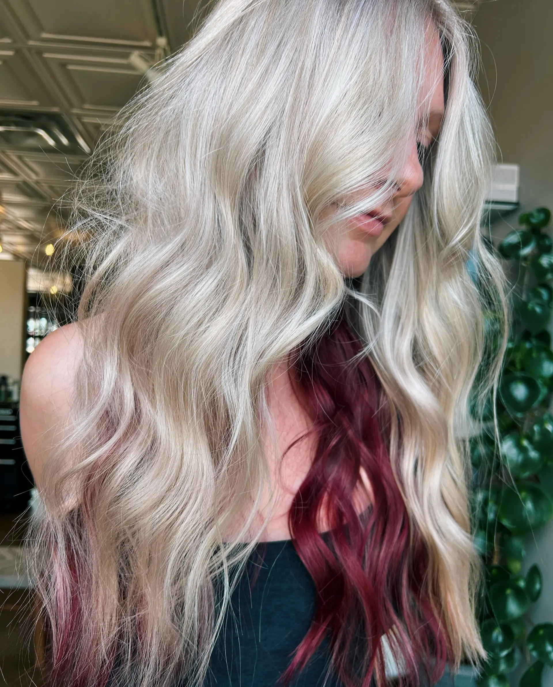 Long wavy platinum blonde hair styled with a hidden layer of rich magenta peekaboo color. 1