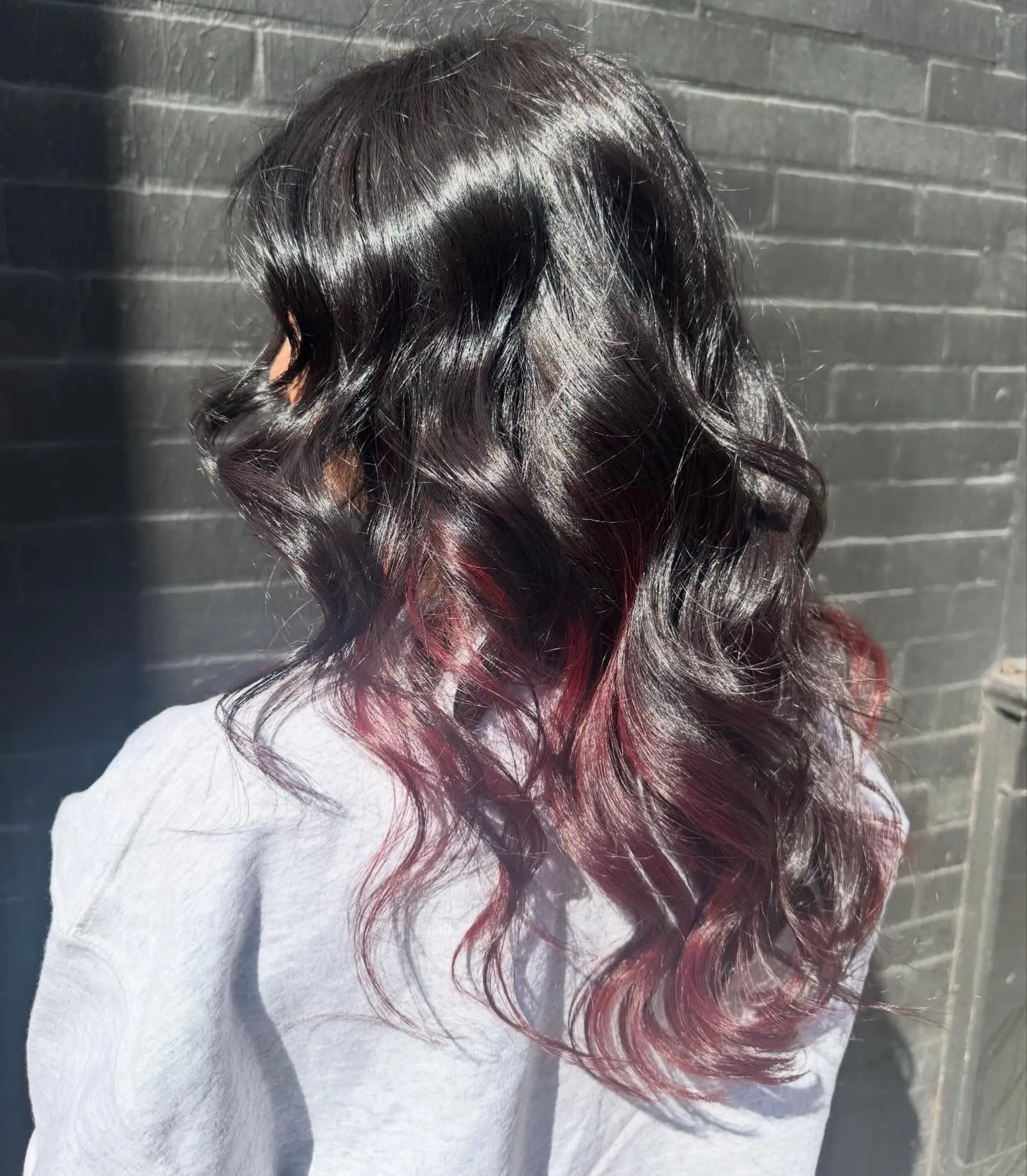Glossy black long hair styled in loose waves featuring vibrant red peekaboo color through the lower layers. 1