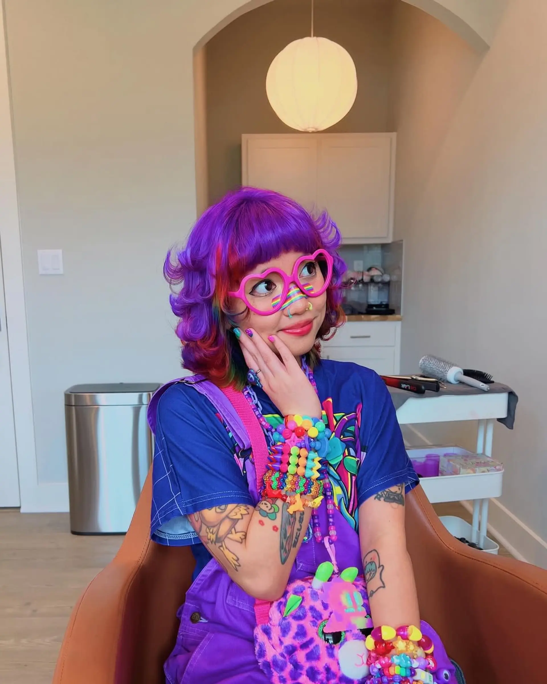 A fun, short curly bob style with bright purple hair on top and a surprise rainbow underlayer, creating a peekaboo effect when the hair moves, offering a dynamic and playful look. 2