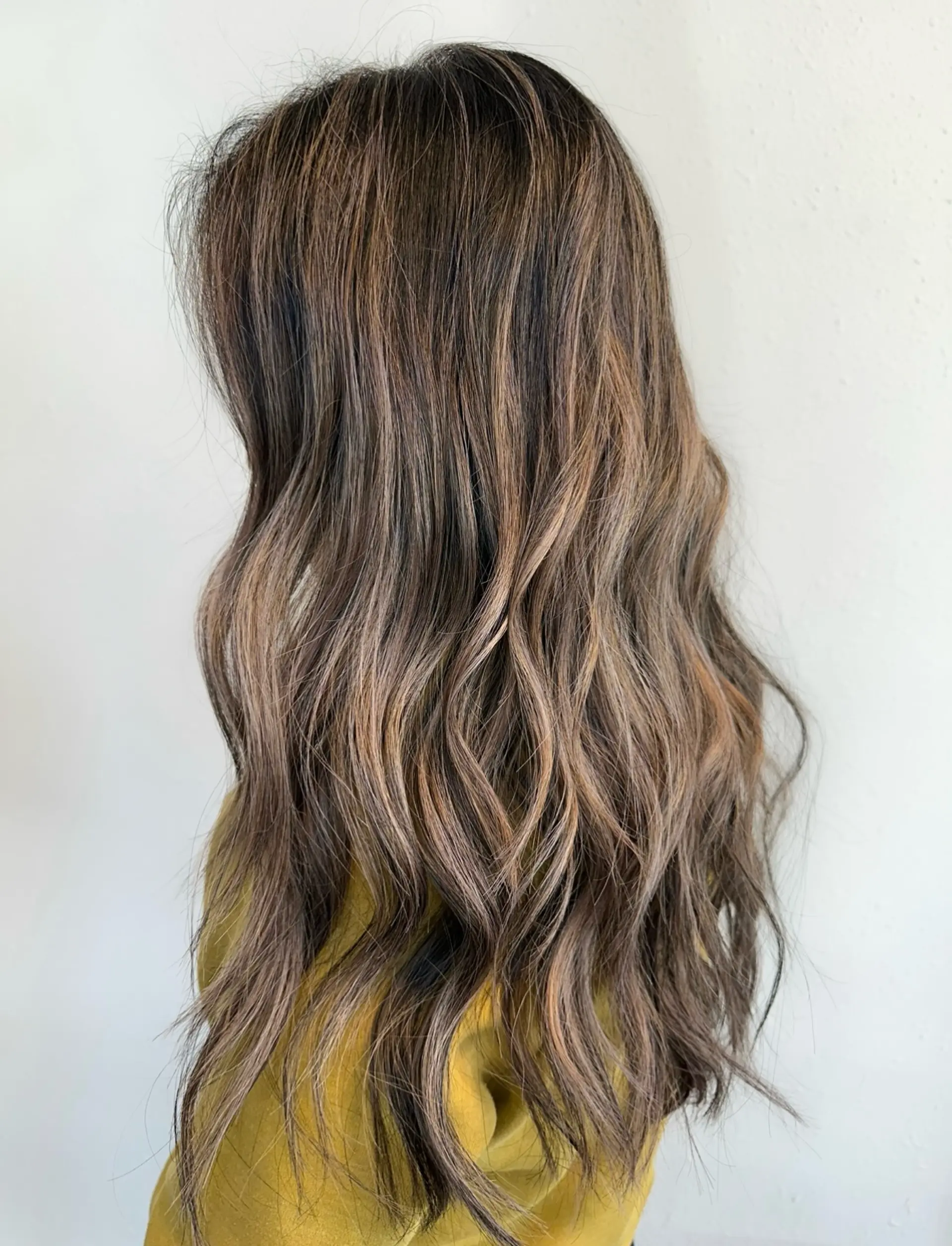 Long dimensional brunette hair with soft caramel highlights styled in textured loose waves. 1