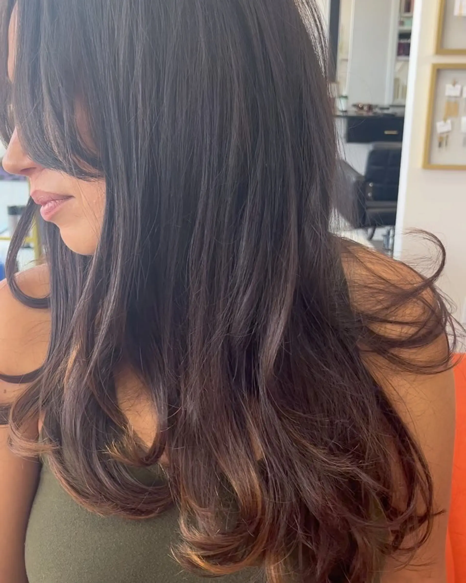 Long dark brunette hair styled into a bouncy, voluminous blowout with flipped ends and face-framing curtain bangs. 1