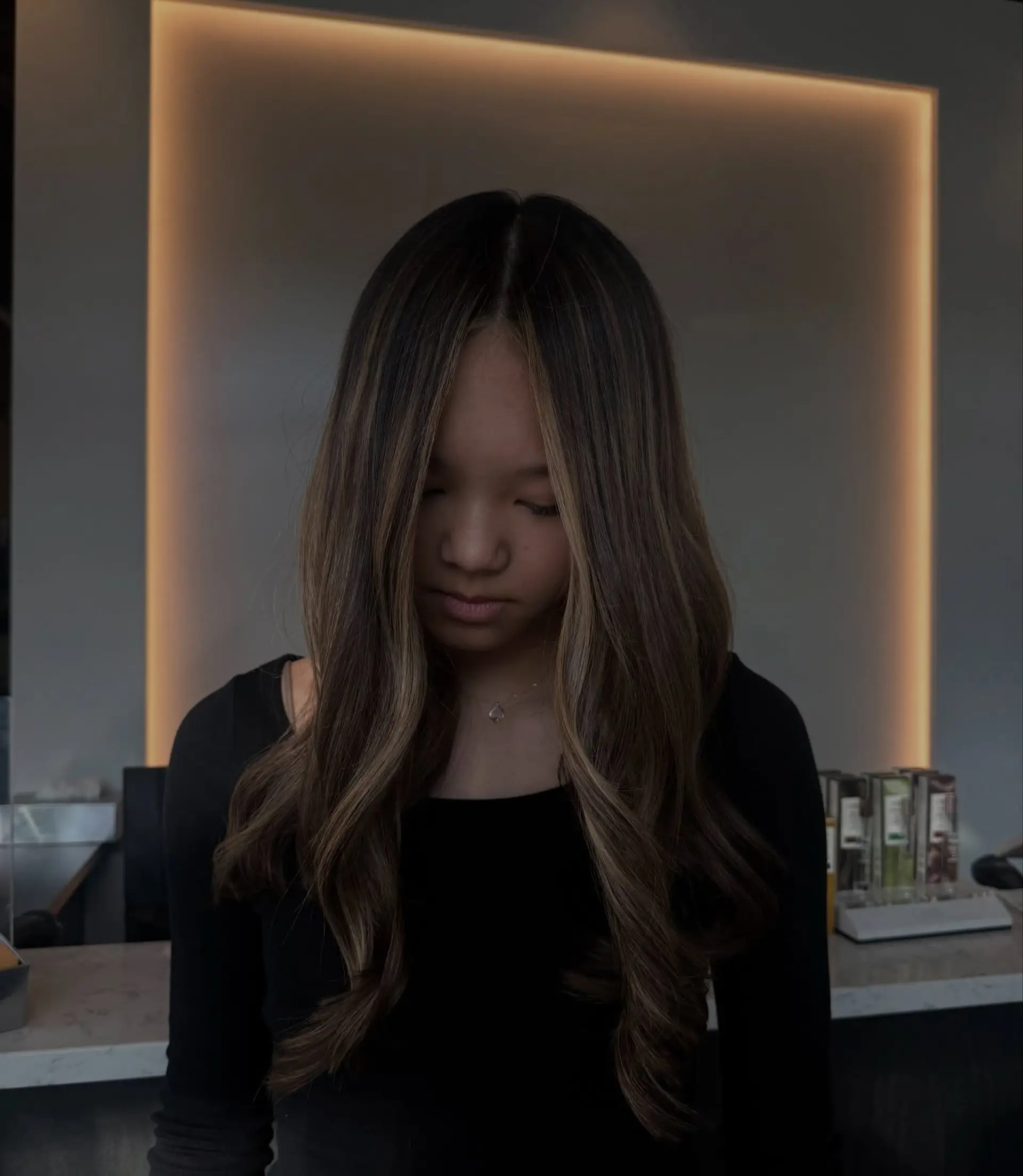 Long dark hair styled into soft, elegant waves featuring warm honey blonde highlights and face-framing dimension. 1