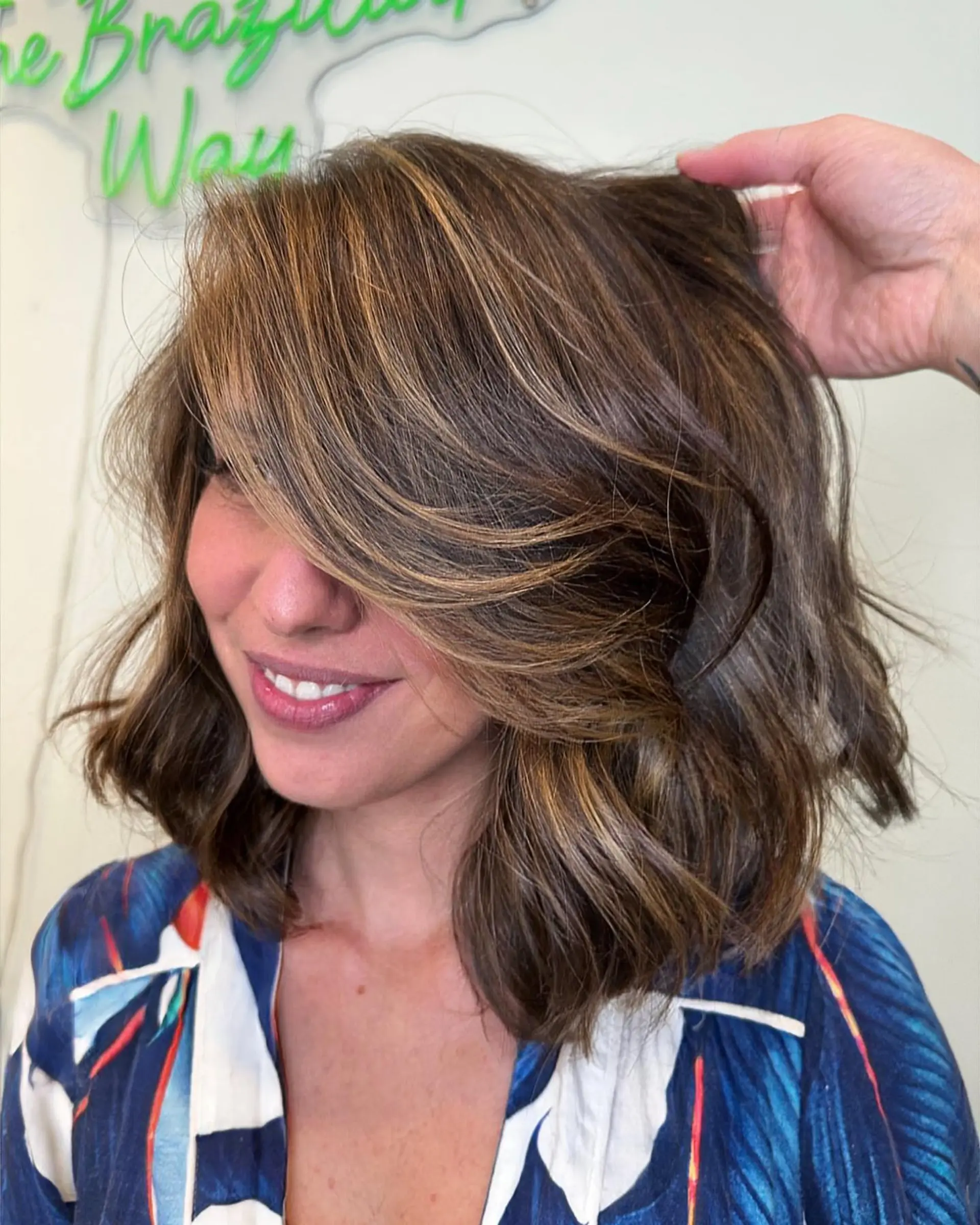 A wavy, textured shoulder-length lob featuring warm caramel highlights and voluminous, sweeping curtain bangs. 1