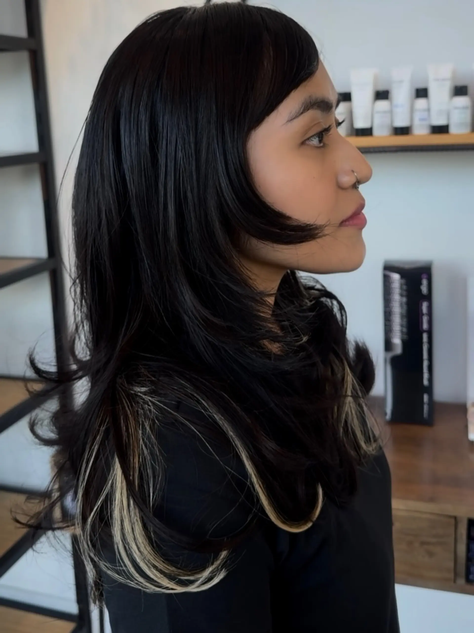 A dark layered haircut featuring side-swept bangs and contrasting blonde peekaboo highlights. 1
