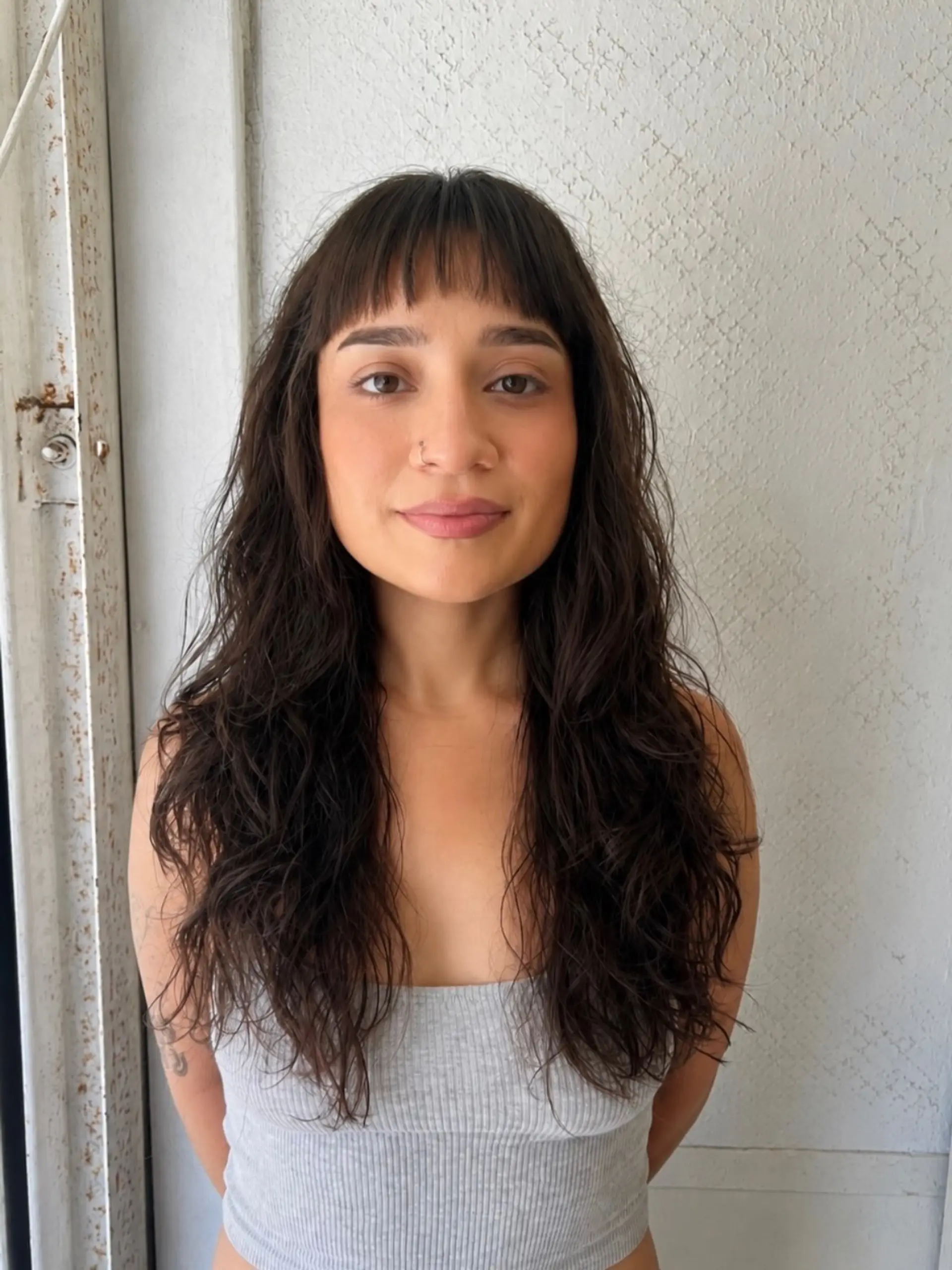 Long dark wavy hair with soft layered texture, framed by short, straight micro bangs. 1