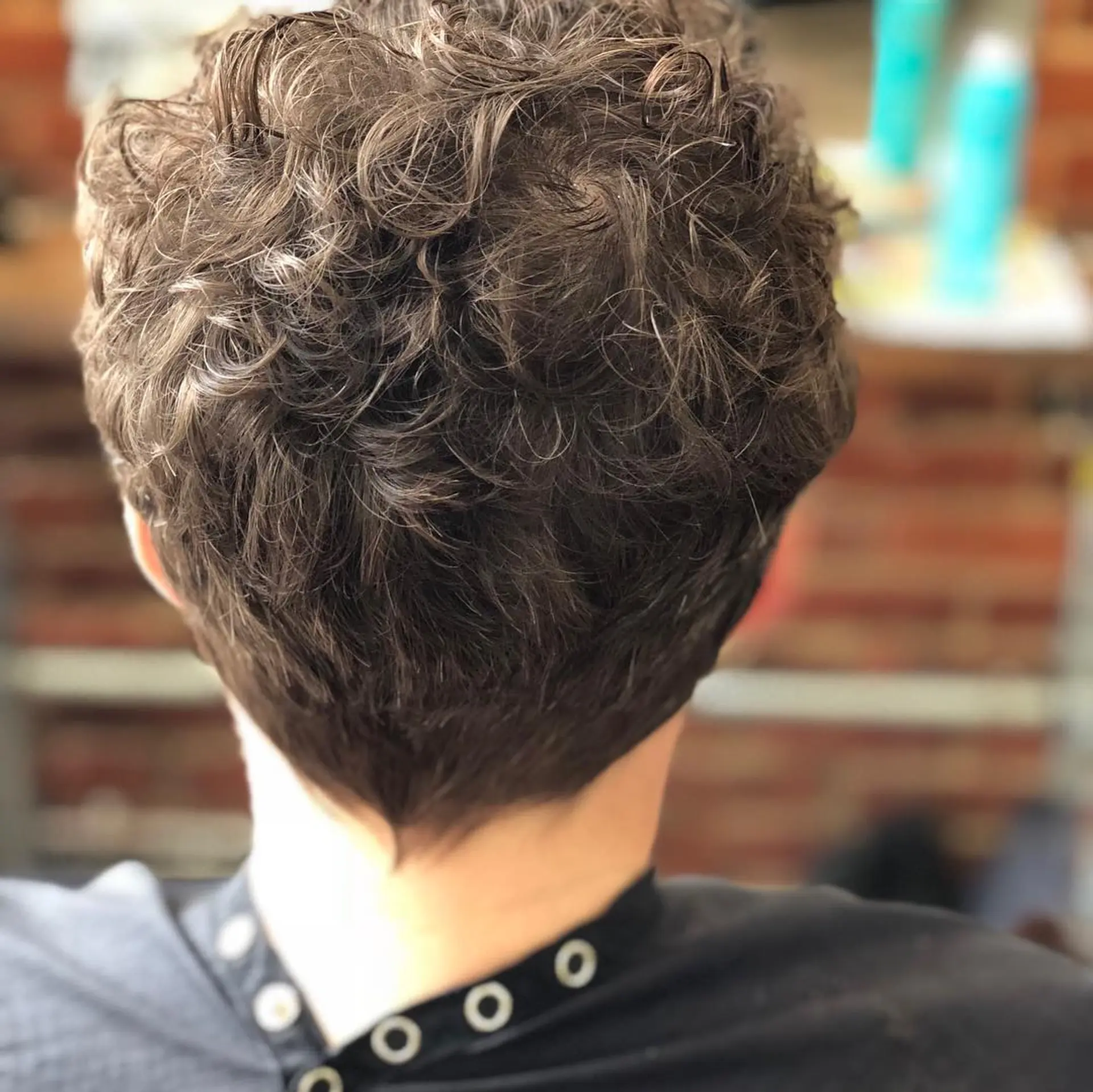 A short, textured curly haircut with natural waves and a softly tapered nape. 1