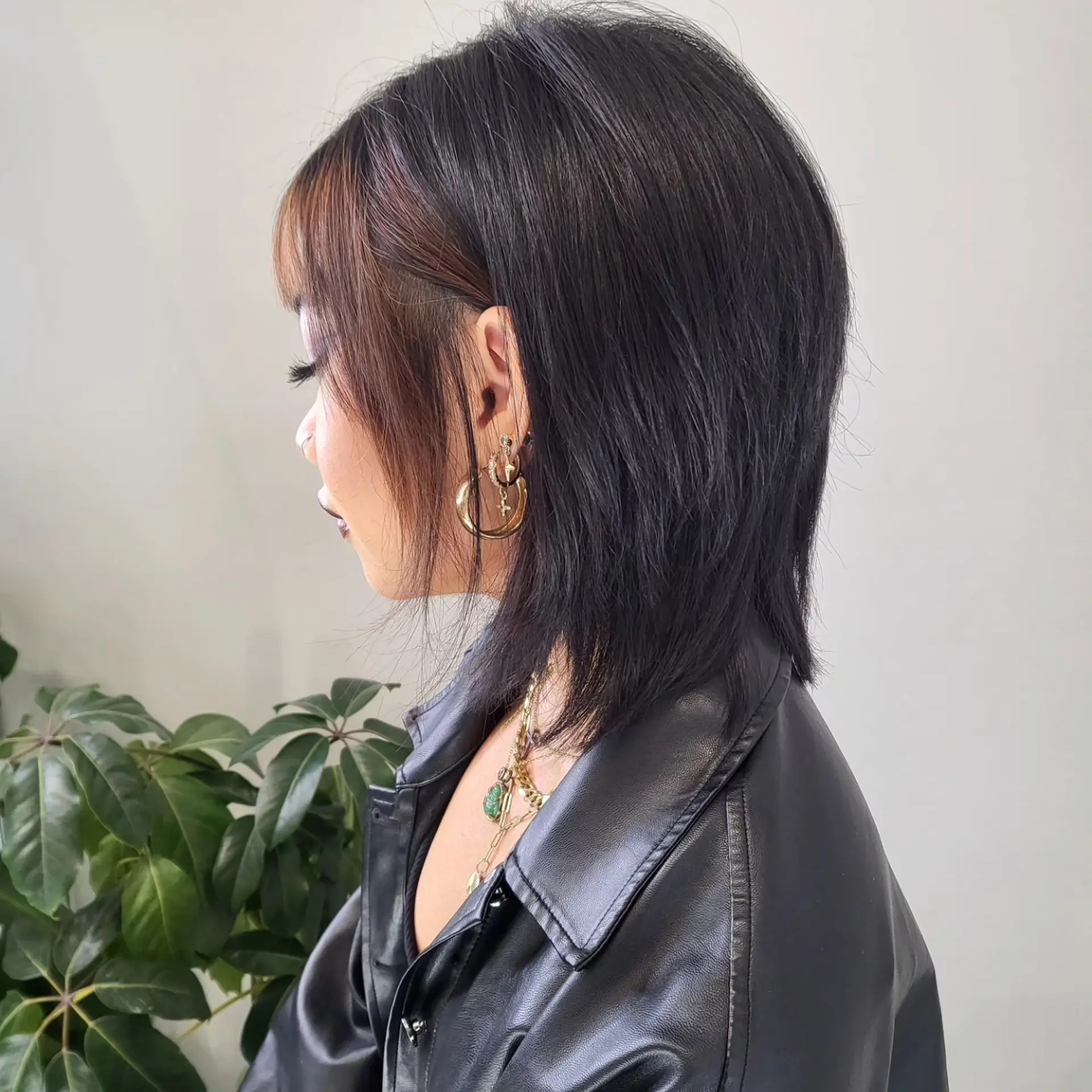 A side-profile view of a textured wolf cut featuring wispy front bangs, face-framing tendrils, and a layered, tapered finish at the collar. 1
