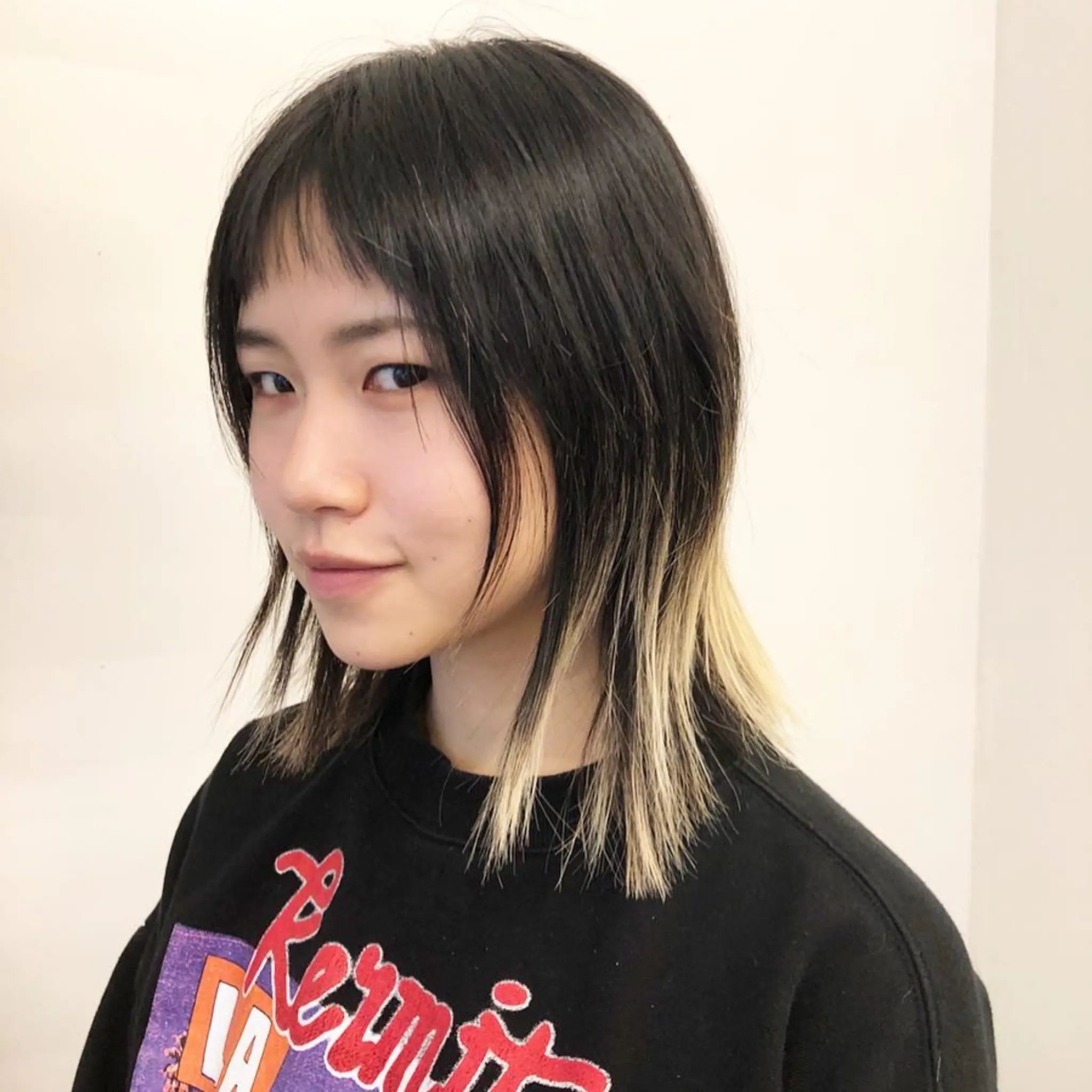A sleek, straight medium-length haircut with black hair and blonde dip-dyed ends, complemented by blunt bangs.