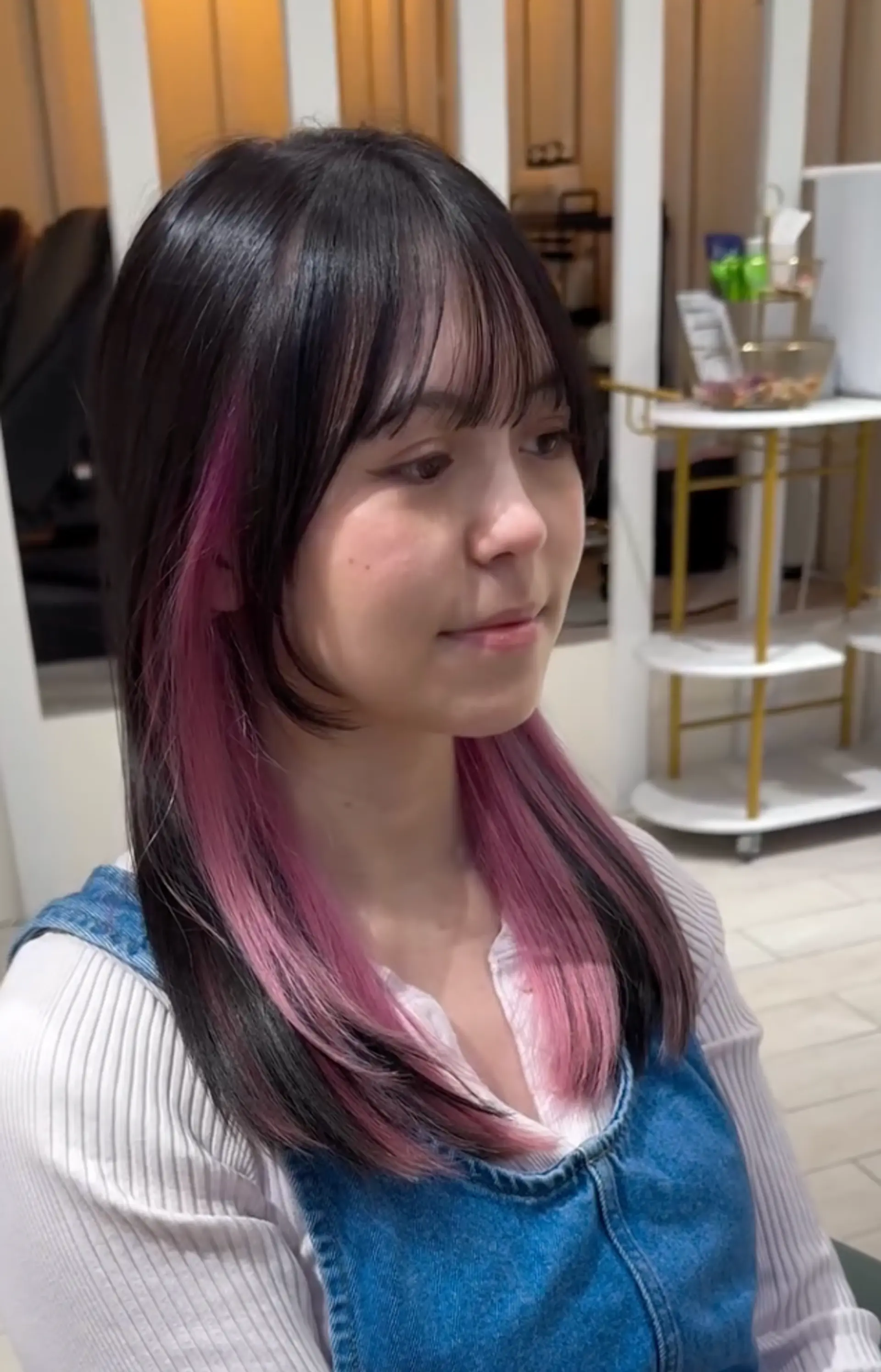 Medium-length straight hair with black roots transitioning to pink ombre ends, blunt bangs, and layered styling.
 2