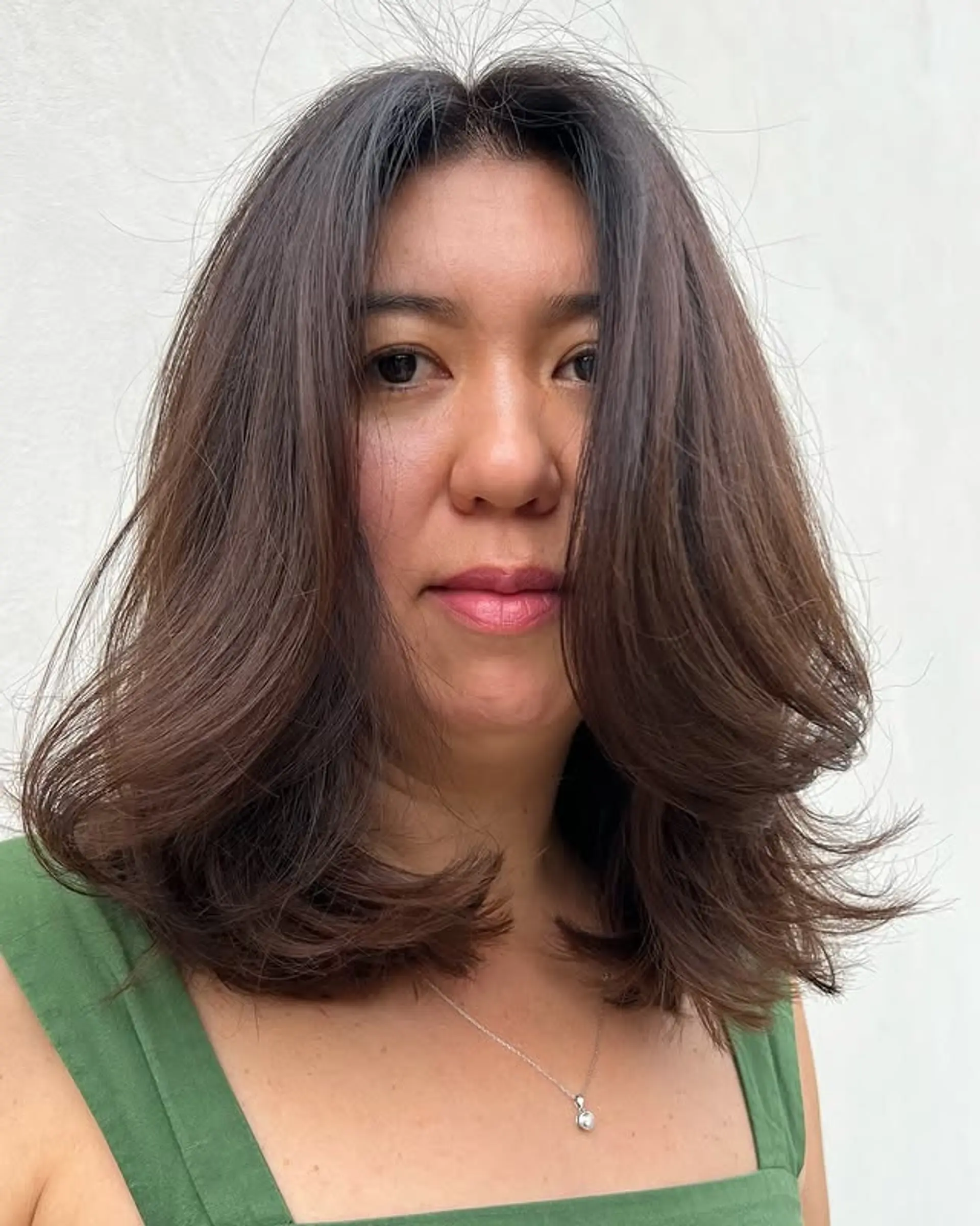 A medium-length layered haircut with curtain bangs, styled with a voluminous blowout. 1