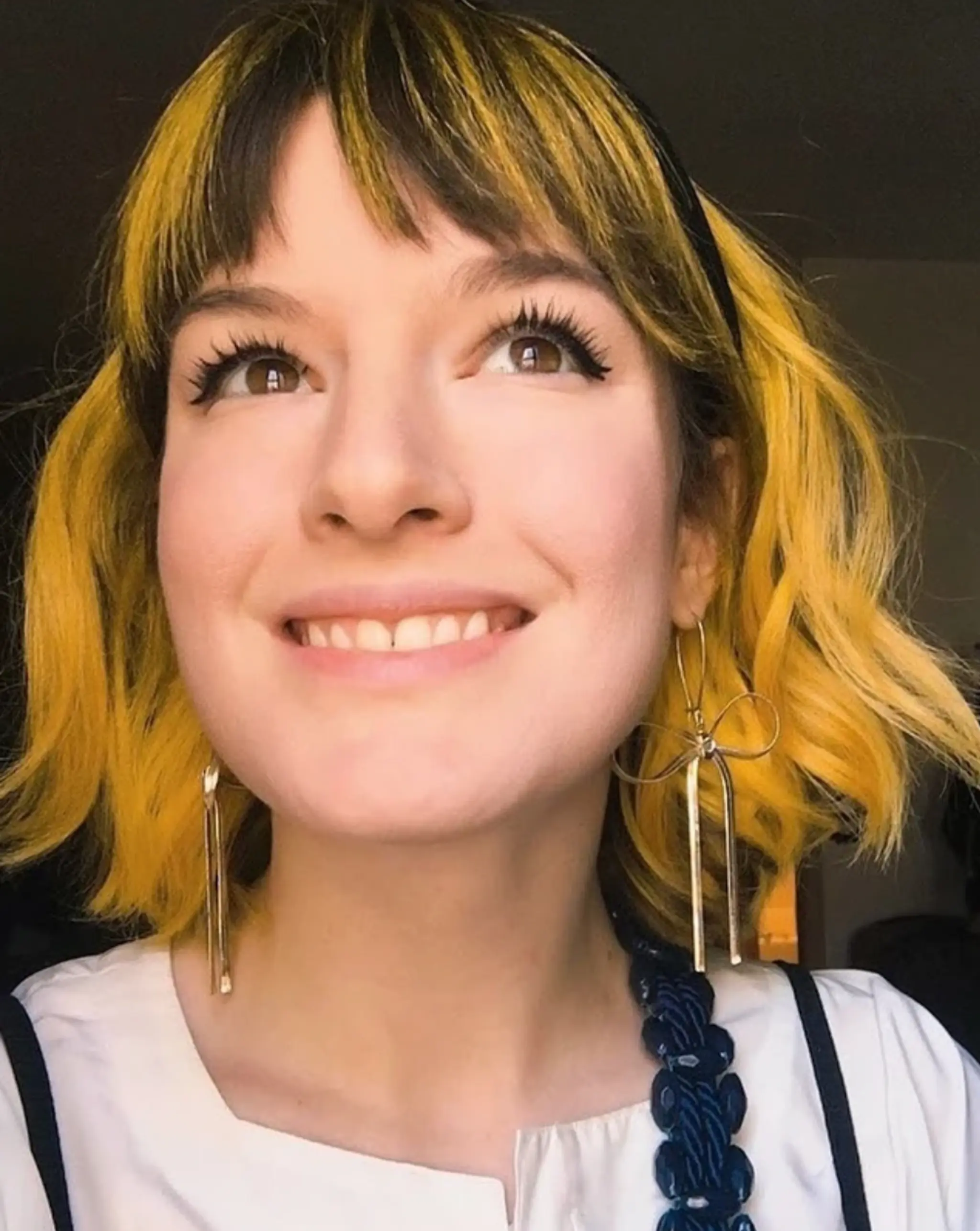 A short wavy bob featuring bright yellow hair with dark roots and a headband accessory.