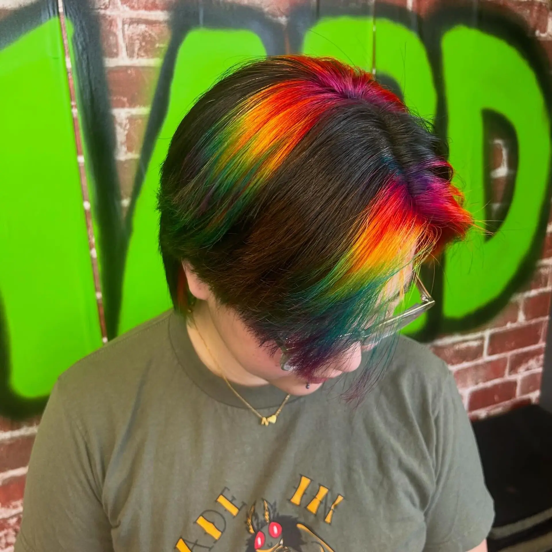 Short dark hair featuring chunky, vivid rainbow prism highlights placed across the fringe and crown. 1