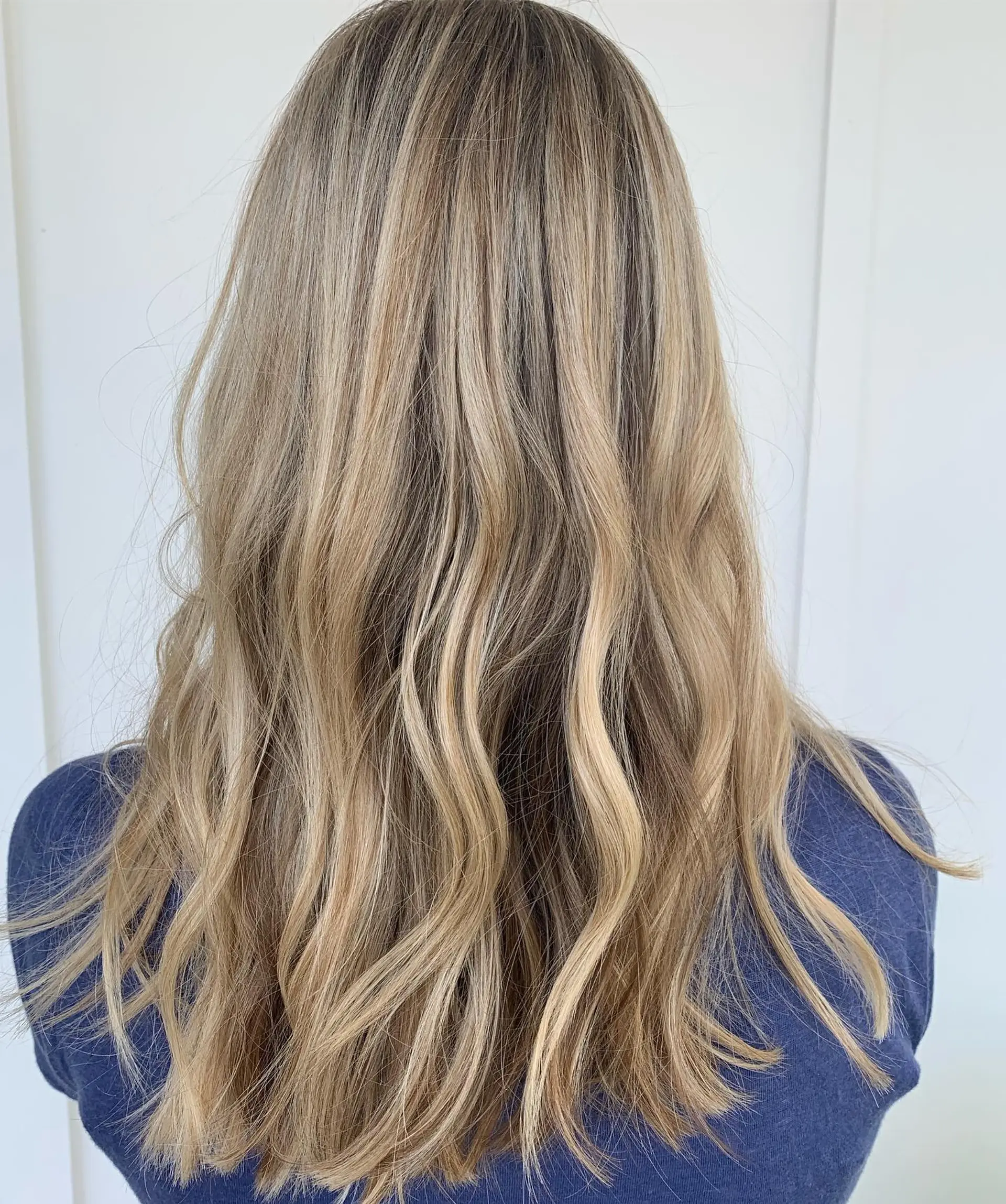 Long, dimensional warm blonde highlighted hair with subtle layers styled into gentle, tousled waves. 1