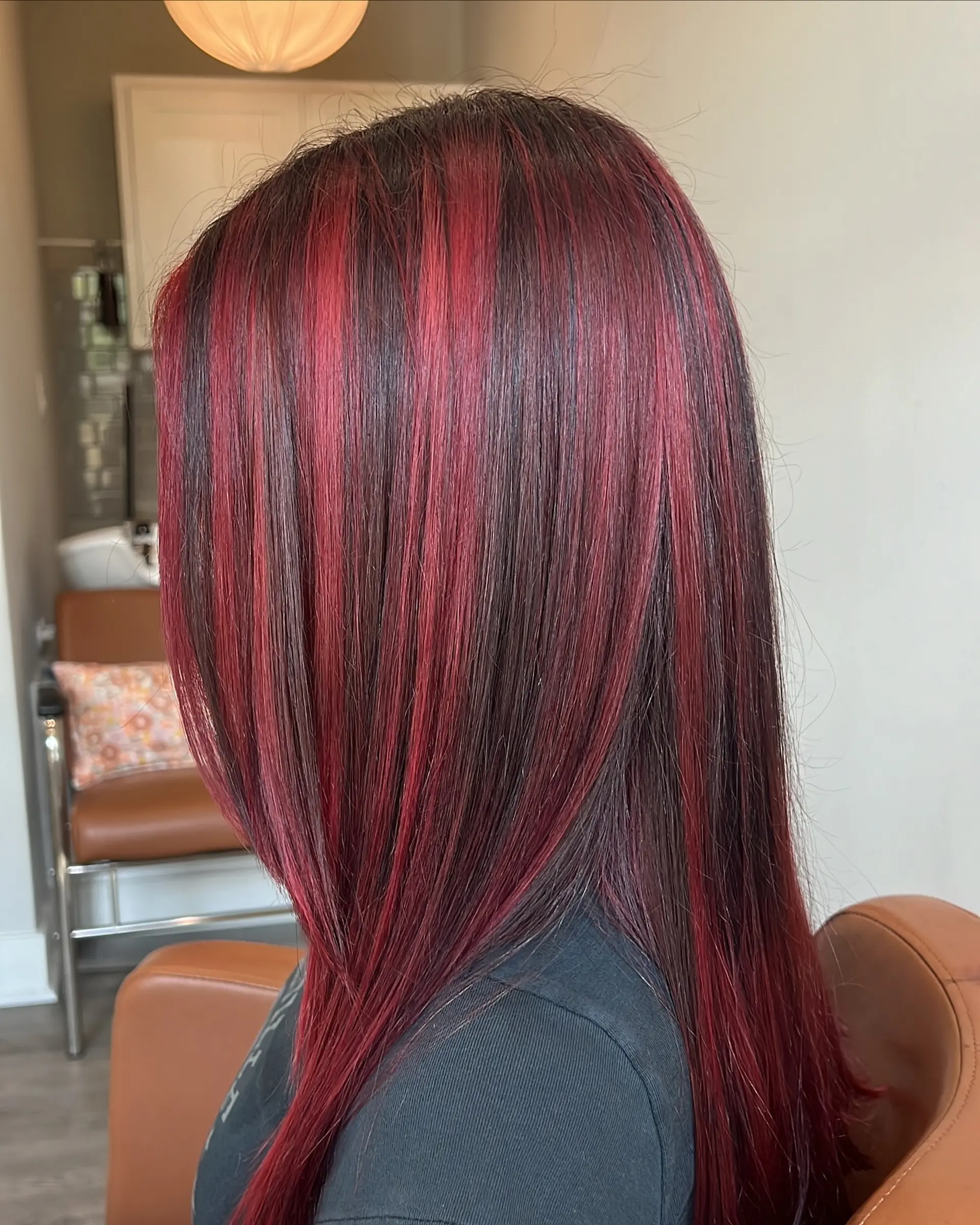 A sleek, long layered haircut adorned with vivid crimson red highlights meticulously placed over a darker base. The straight strands showcase the vibrant color contrast and natural movement, offering a dimensional and eye-catching look. 3