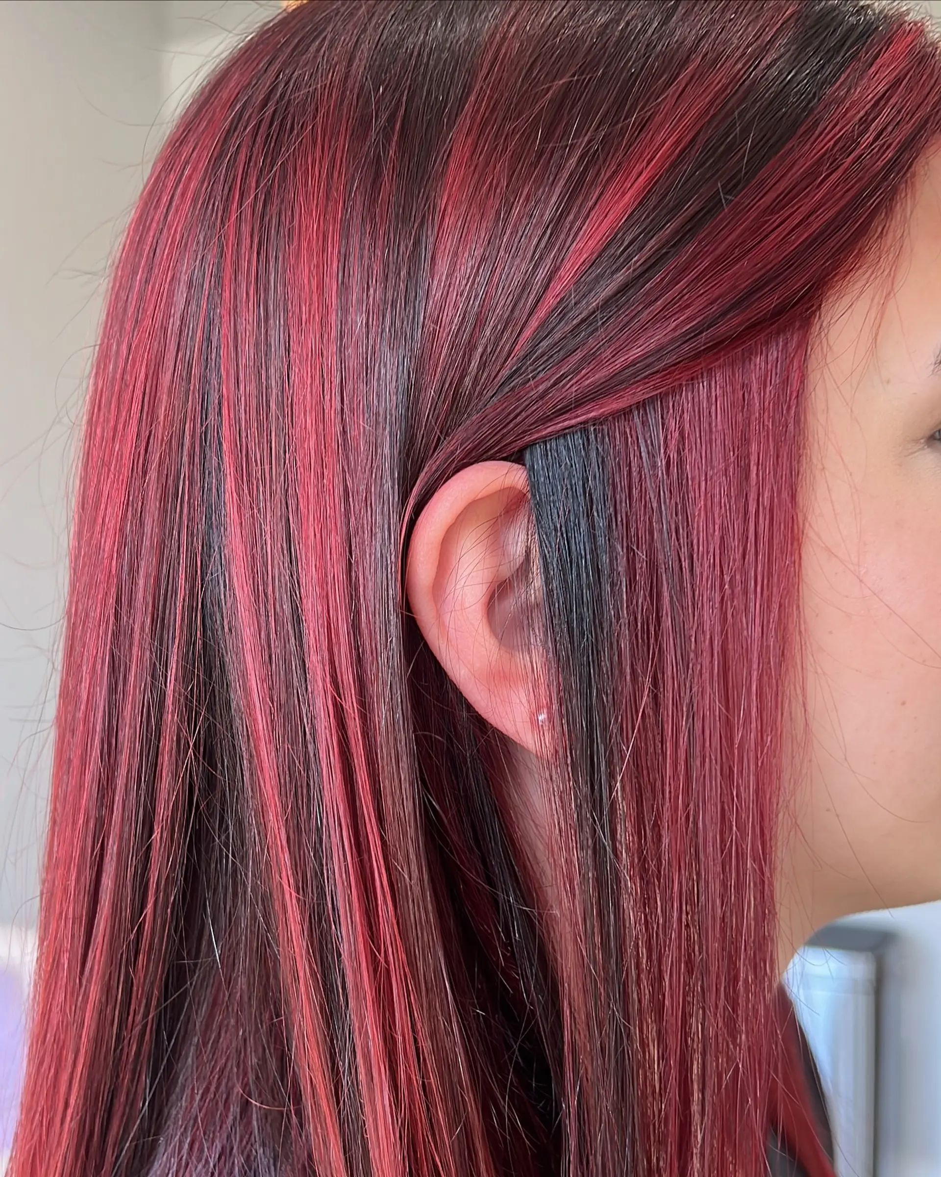 A sleek, long layered haircut adorned with vivid crimson red highlights meticulously placed over a darker base. The straight strands showcase the vibrant color contrast and natural movement, offering a dimensional and eye-catching look. 5