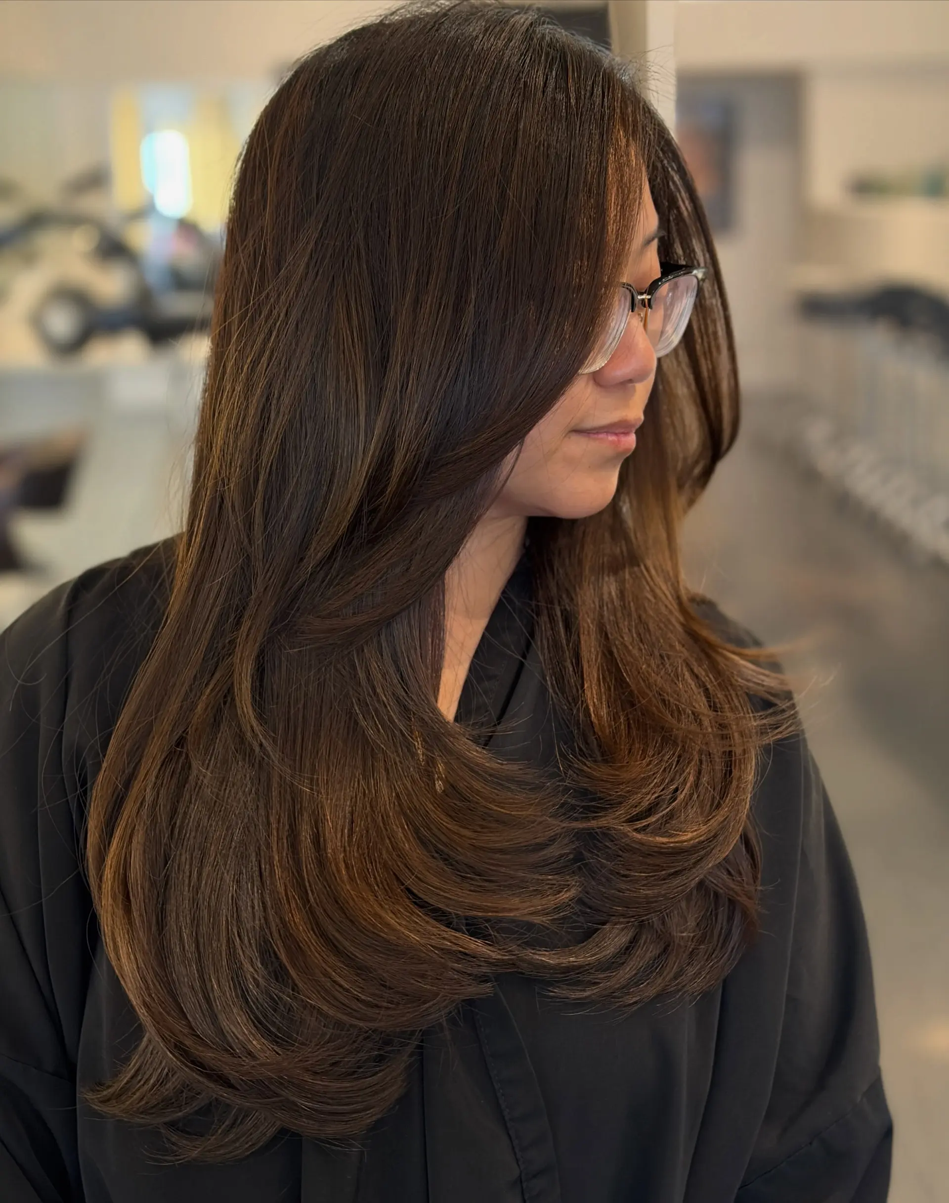 Long dark brown hair cut with soft, sweeping layers and styled into a voluminous blowout with turned-in ends. 1