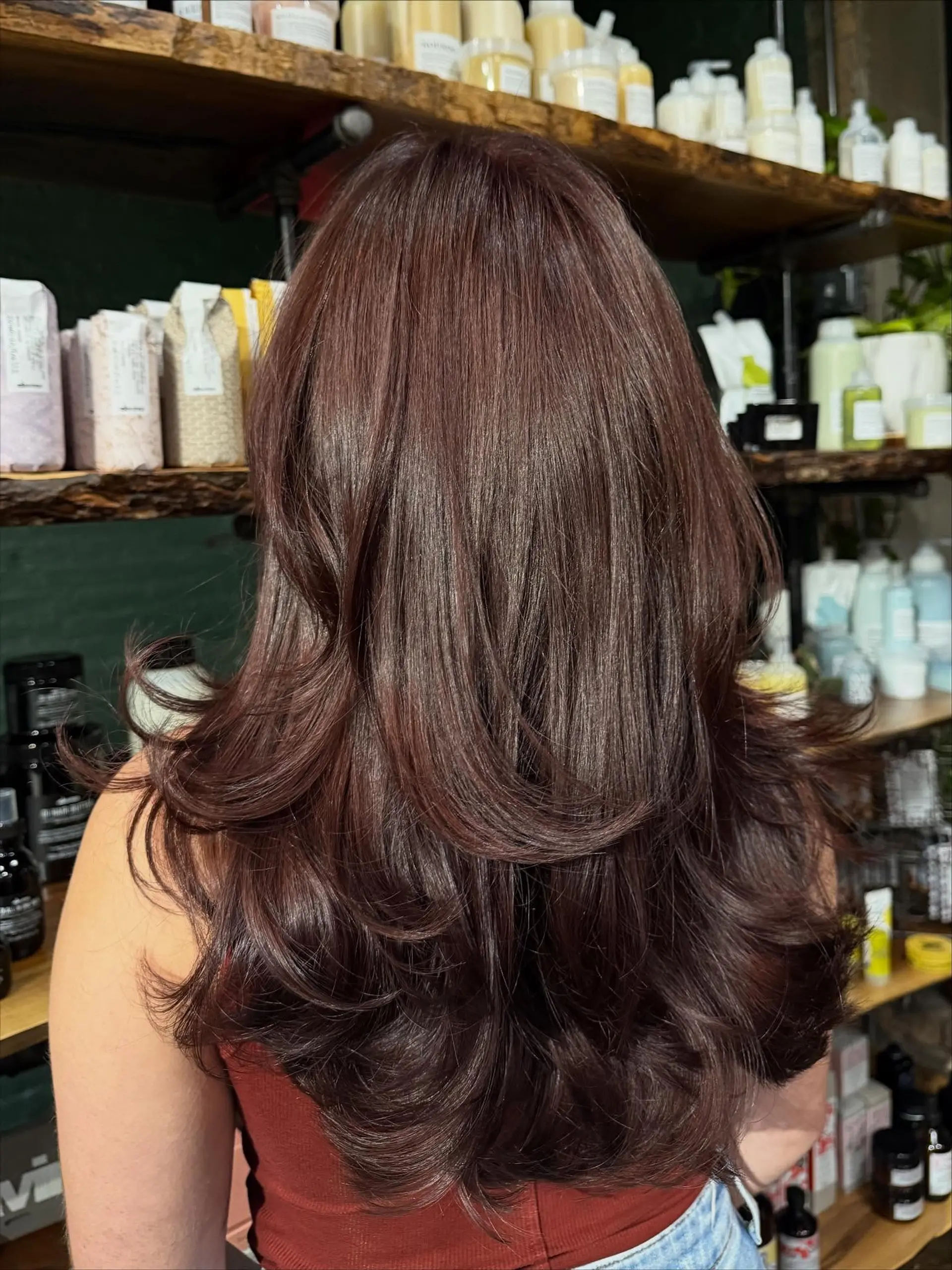 A long, richly toned dark auburn haircut with cascading layers styled into curved, voluminous ends. 1