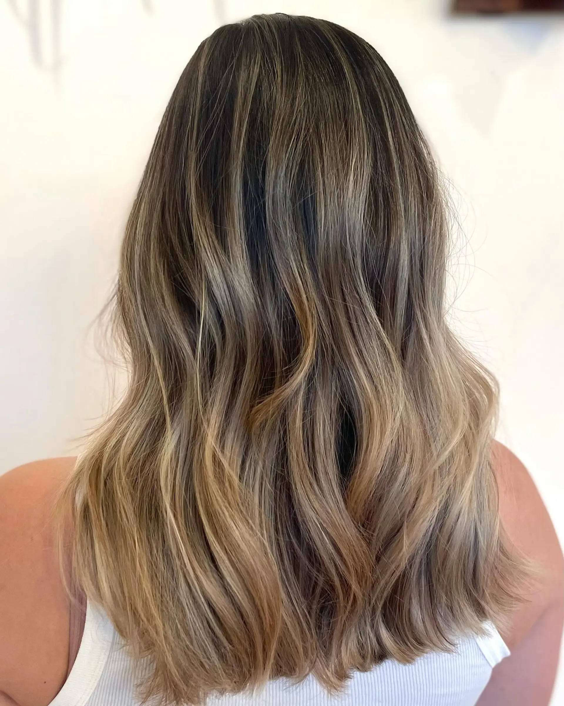 Medium-length dimensional bronde hair styled with soft, loose waves and natural rooted highlights. 1