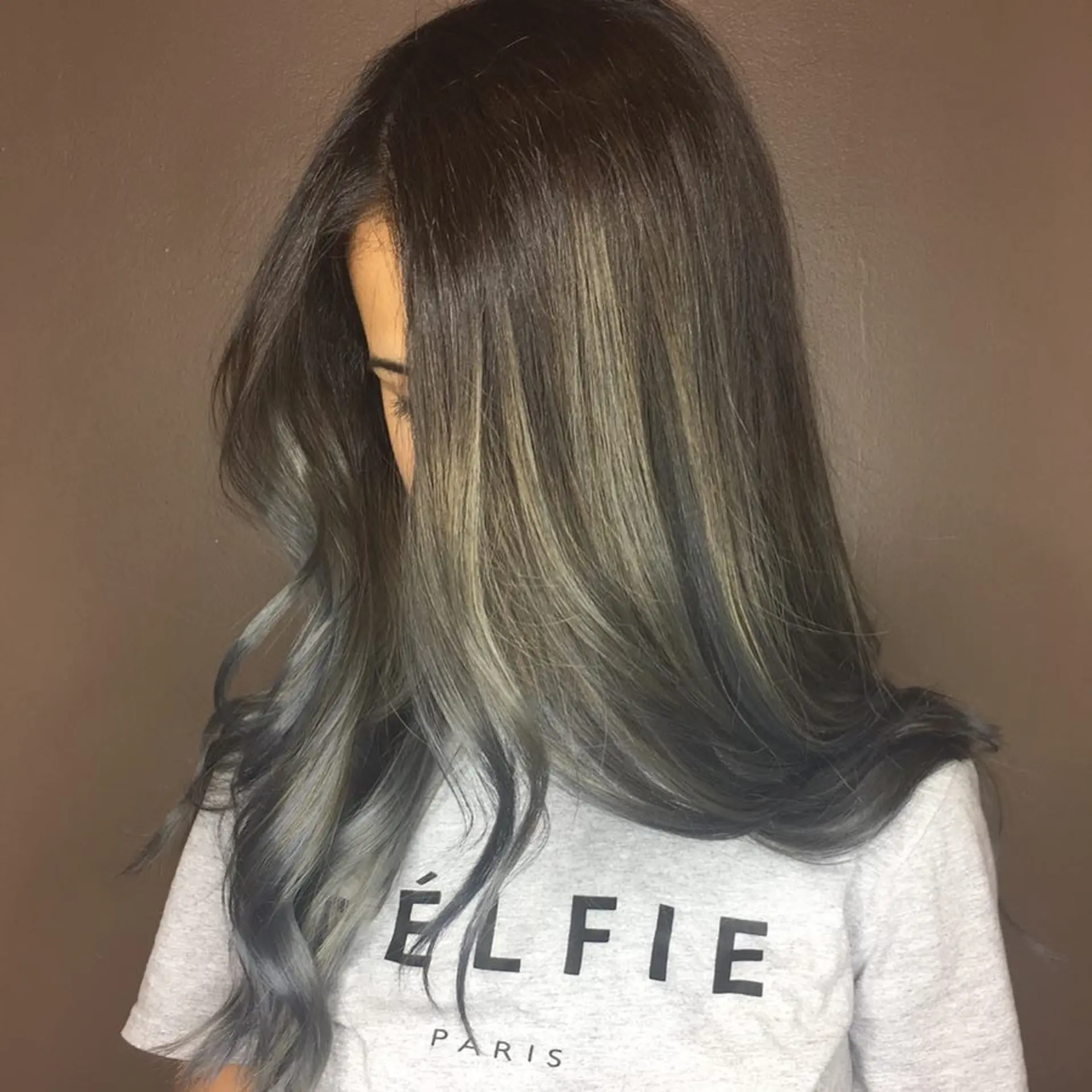 Long smooth hair styled with soft flowing waves, featuring smoky ash and cool denim/steel blue balayage highlights over a dark root base. 1
