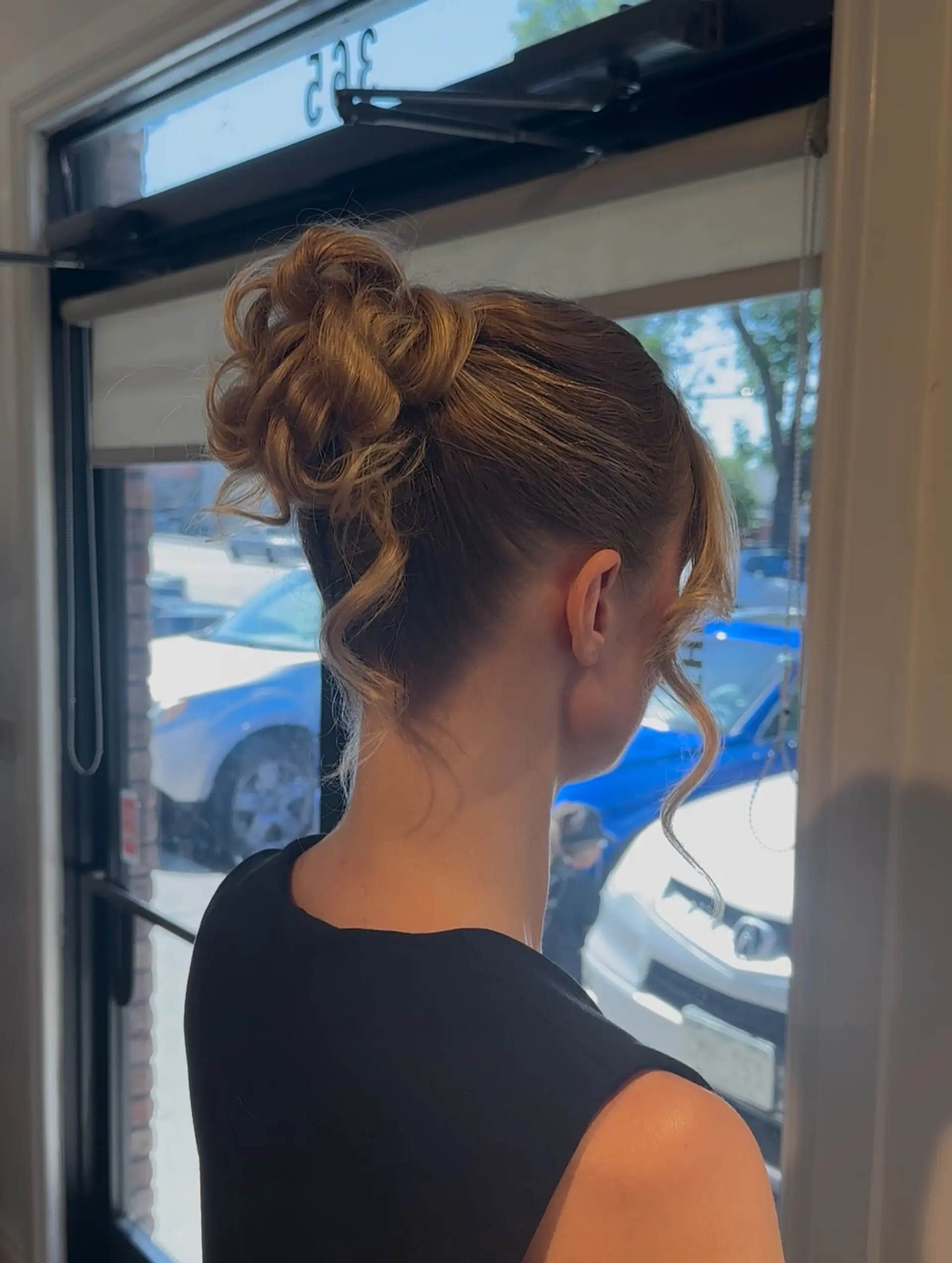 A textured high bun updo featuring soft pinned curls and delicate, face-framing tendrils. 1
