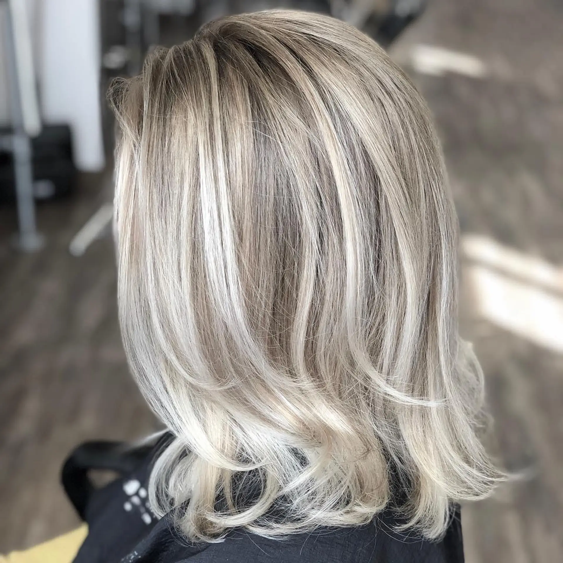A textured medium-length cut featuring a multi-dimensional champagne blonde balayage with a soft shadow root and flipped ends. 1