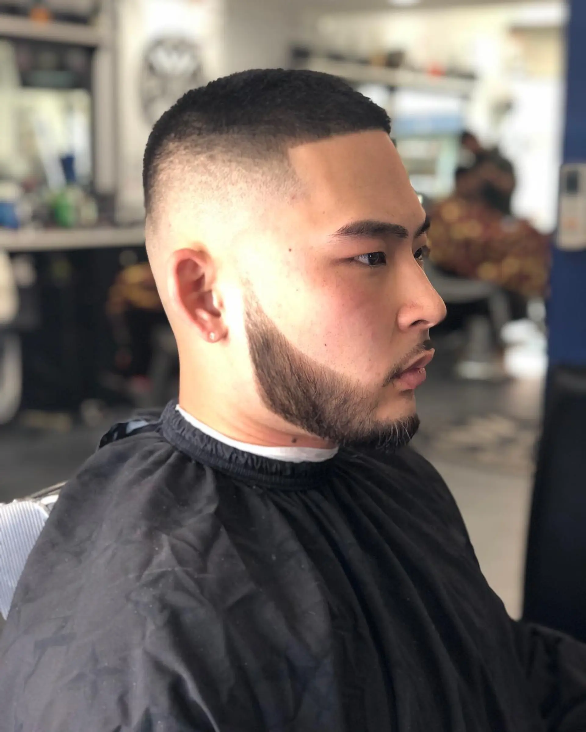 A precise buzz cut paired with a high skin fade, sharp hairline shape-up, and a blended beard. 1