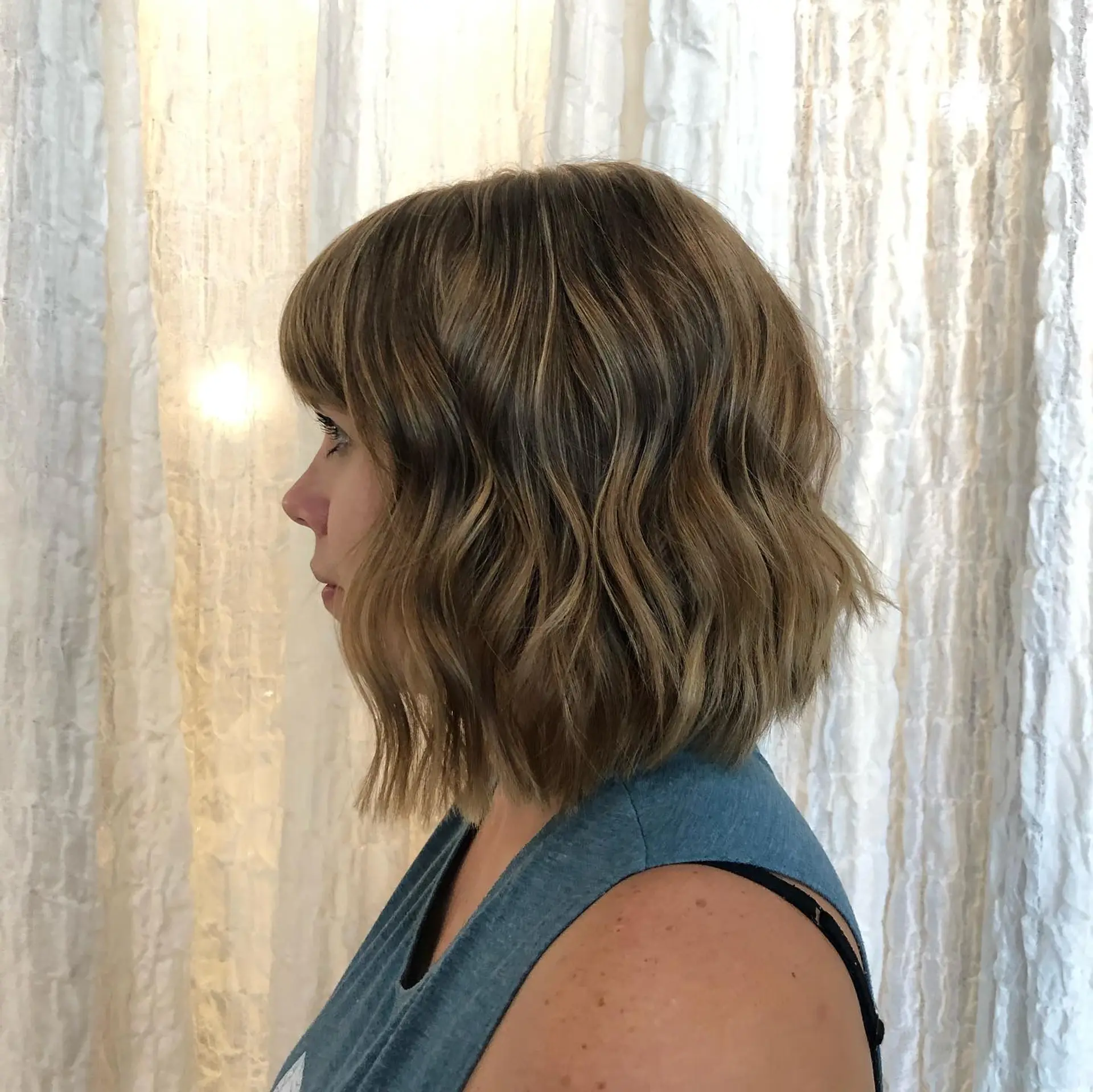 A textured wavy bob haircut featuring fringe bangs and subtle, natural-toned babylights. 1