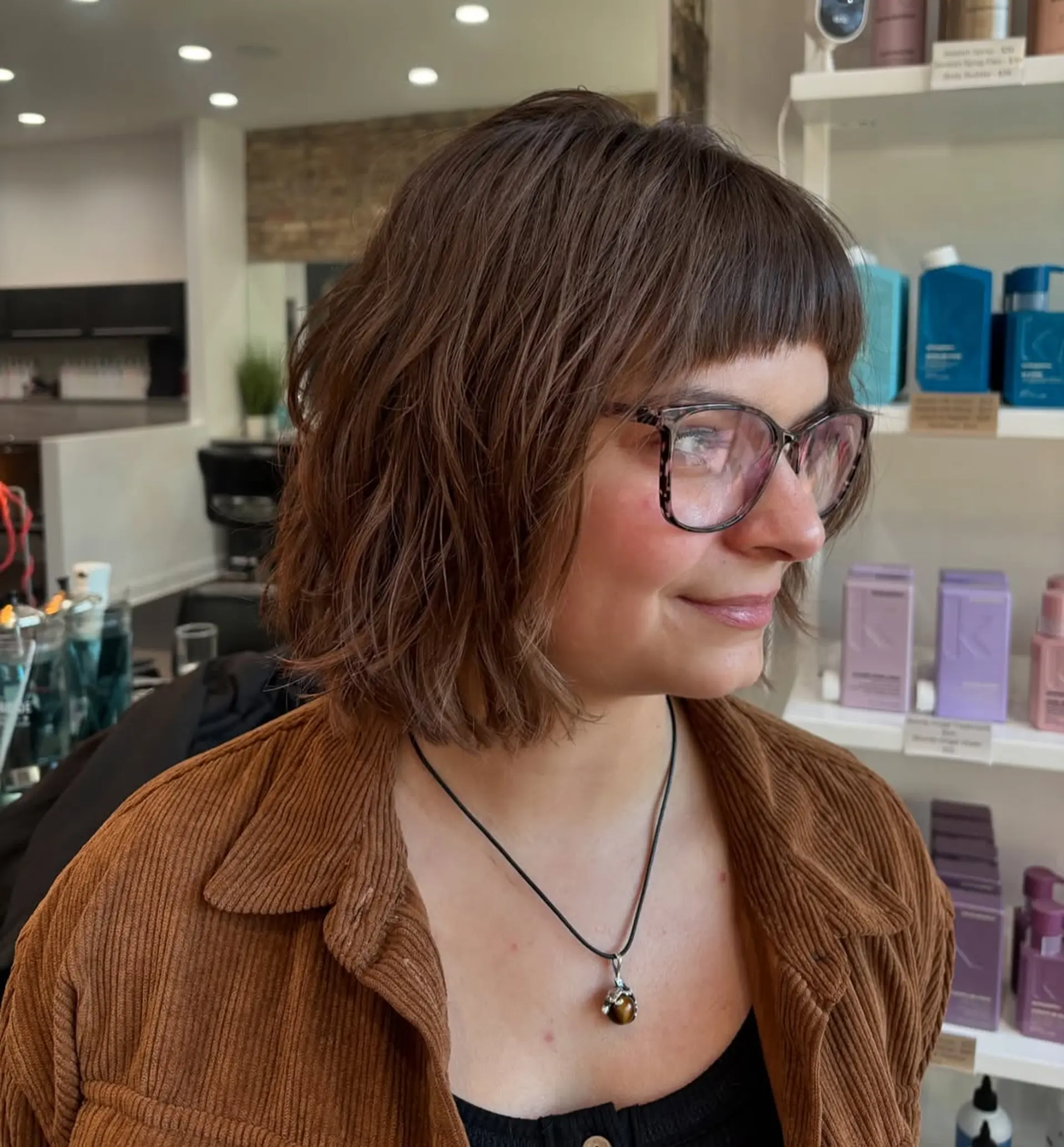 A trendy short wavy bob featuring textured, choppy layers and a distinctive micro fringe. The chin-length cut offers a modern, playful, and easy-to-manage style. 1