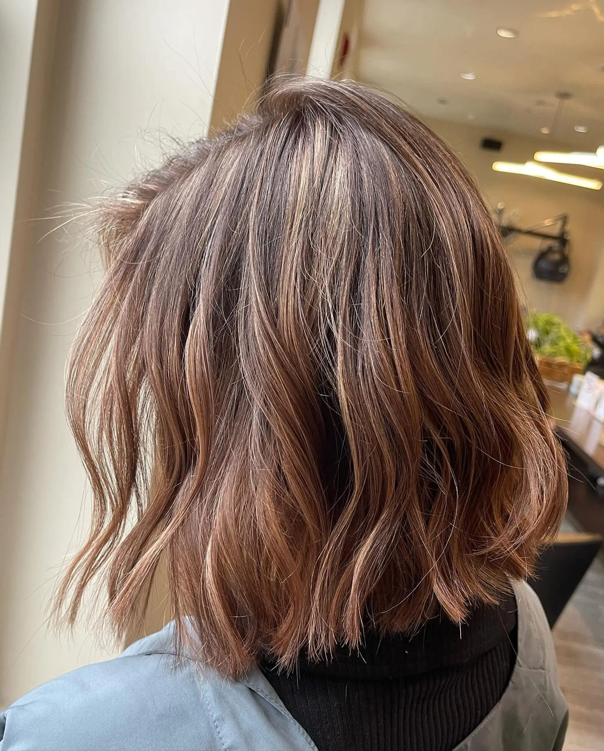 A textured, neck-length bob styled with soft, undone waves and dimensional caramel highlights. 1