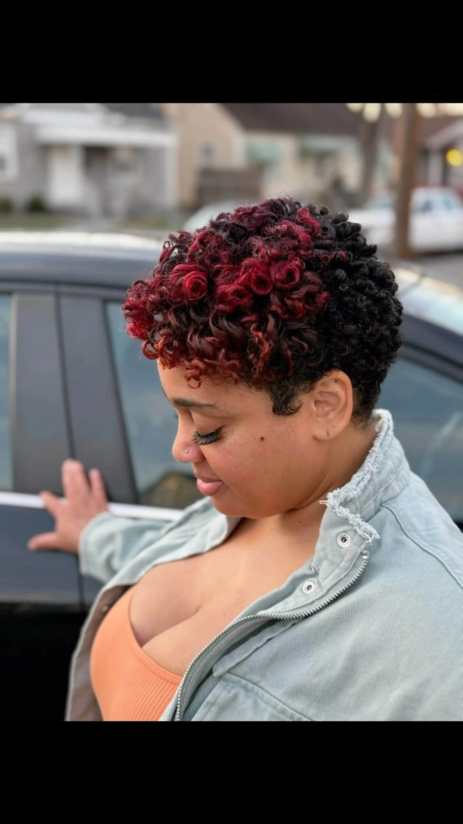 A cropped, tapered curly pixie cut styled with defined curls on top and vibrant sunset red color accents. 1