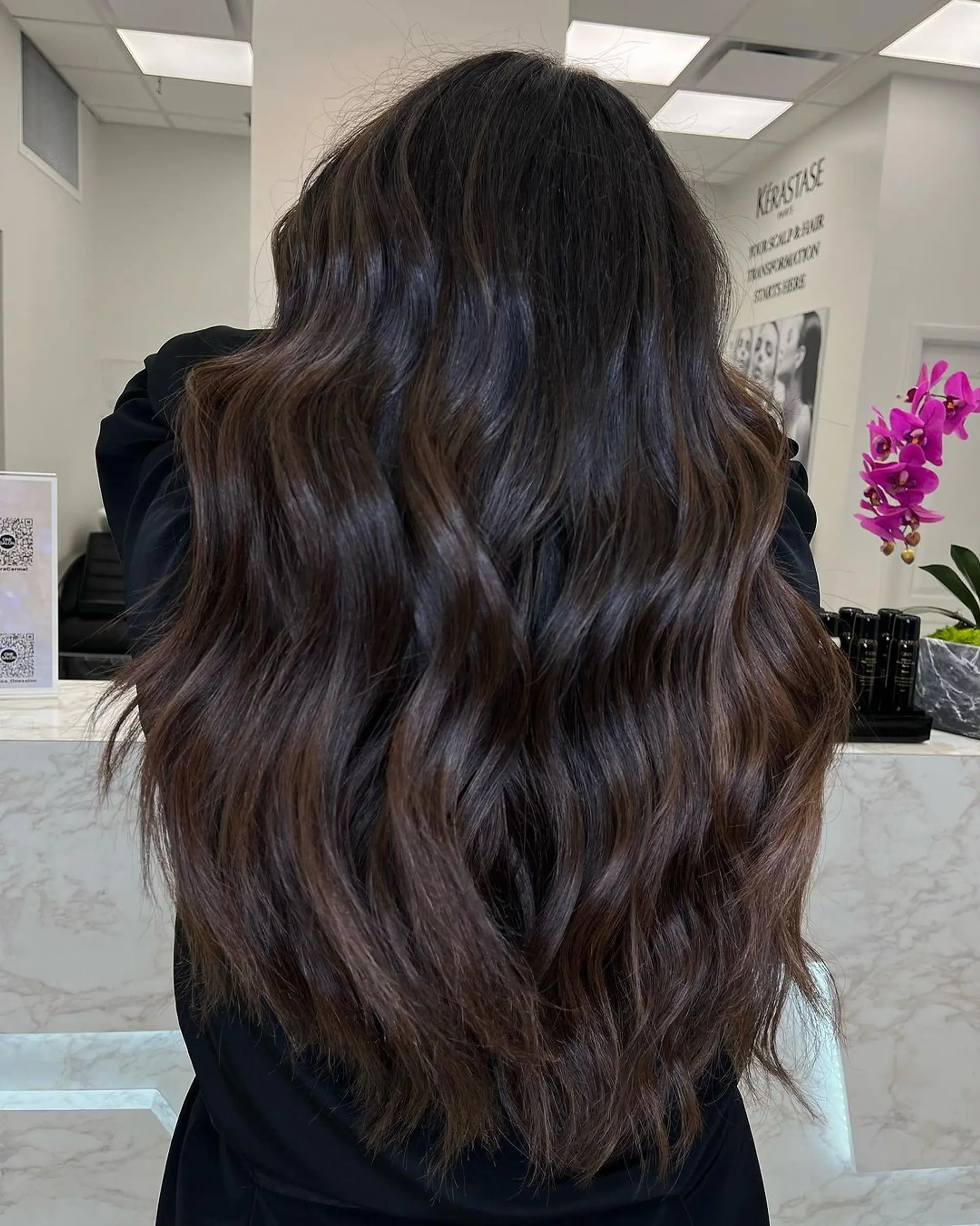 Natural wavy hair that is very long and features dark brown with chestnut highlights, offering a voluminous and shiny finish. 1