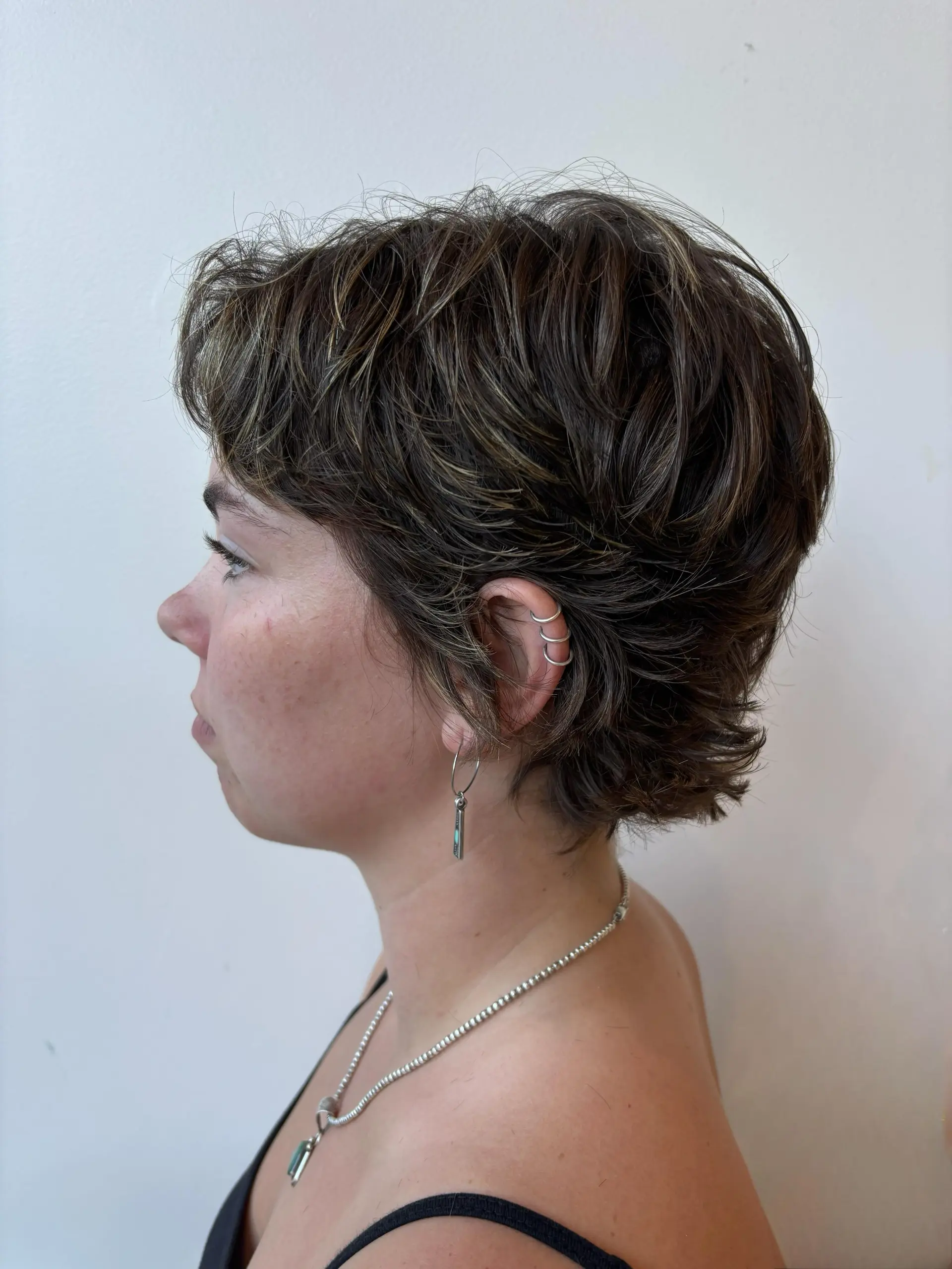 A layered, textured short pixie cut with soft piecey fringe and dimensional brunette tones. 1