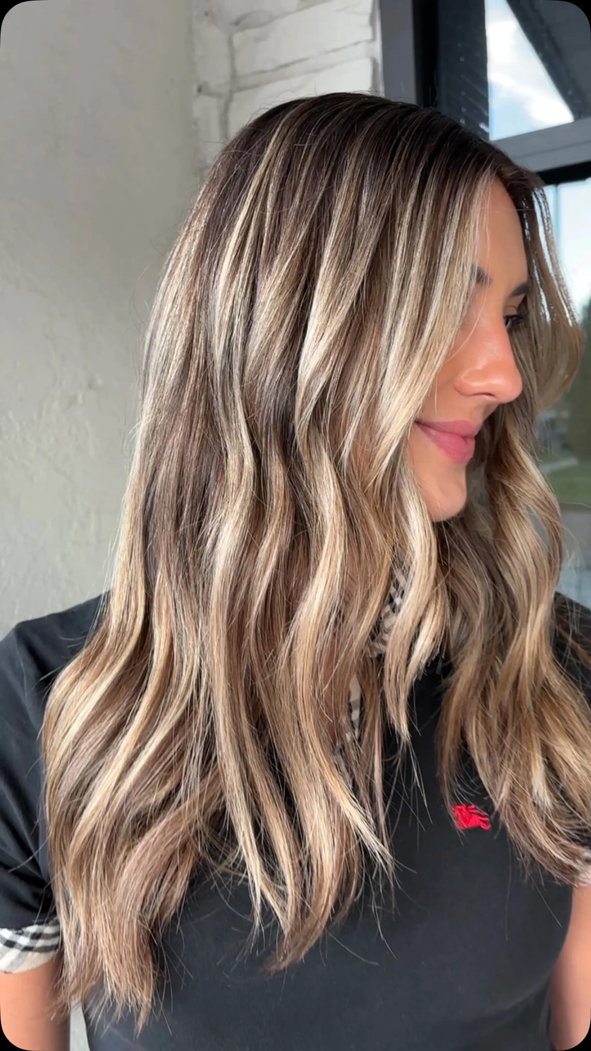Long hair styled with gentle waves, featuring dimensional blonde highlights seamlessly woven over a natural brunette base with bright face-framing accents. 1