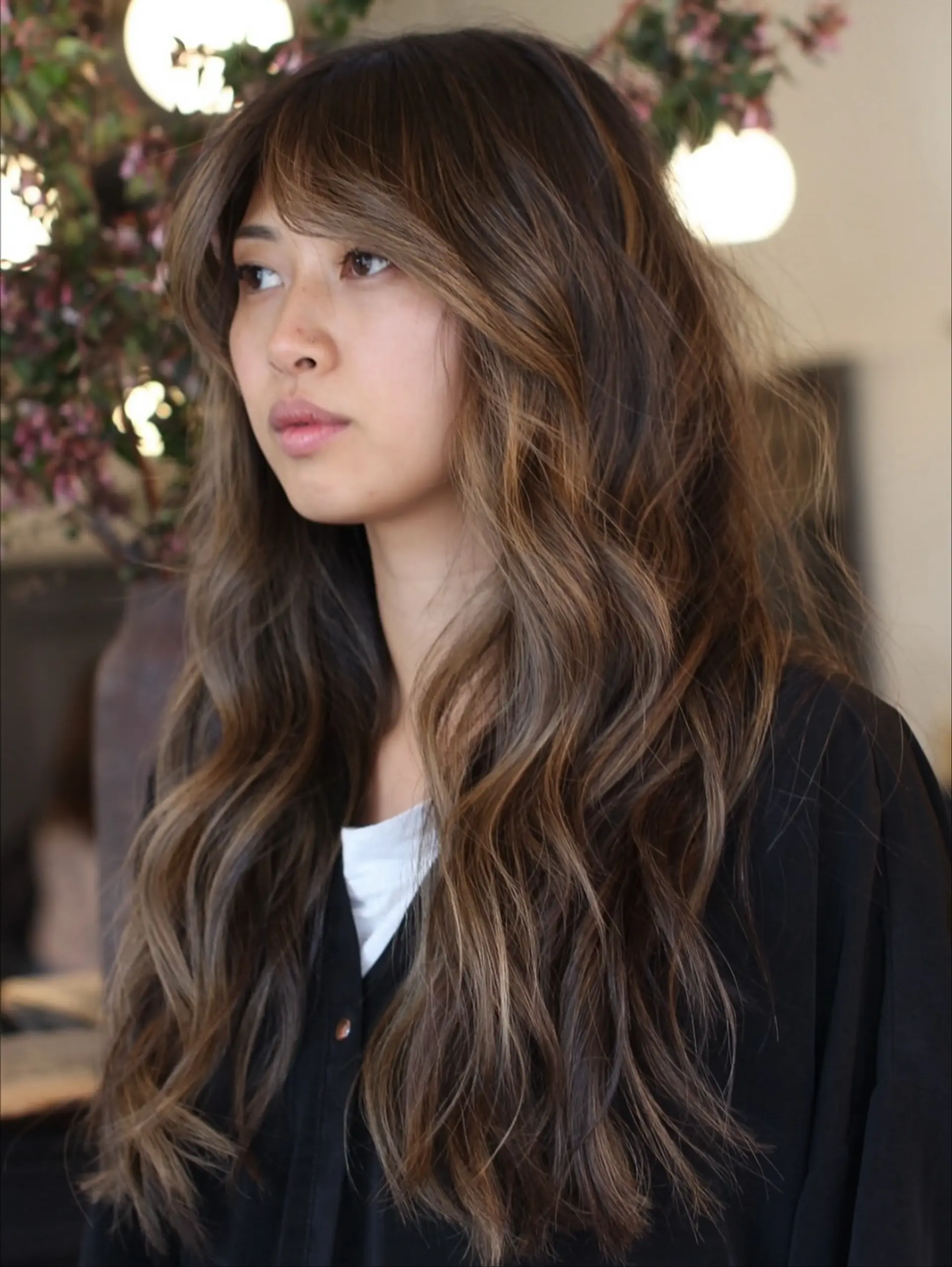 Long wavy dark brown hair featuring warm caramel highlights and face-framing curtain bangs. 1