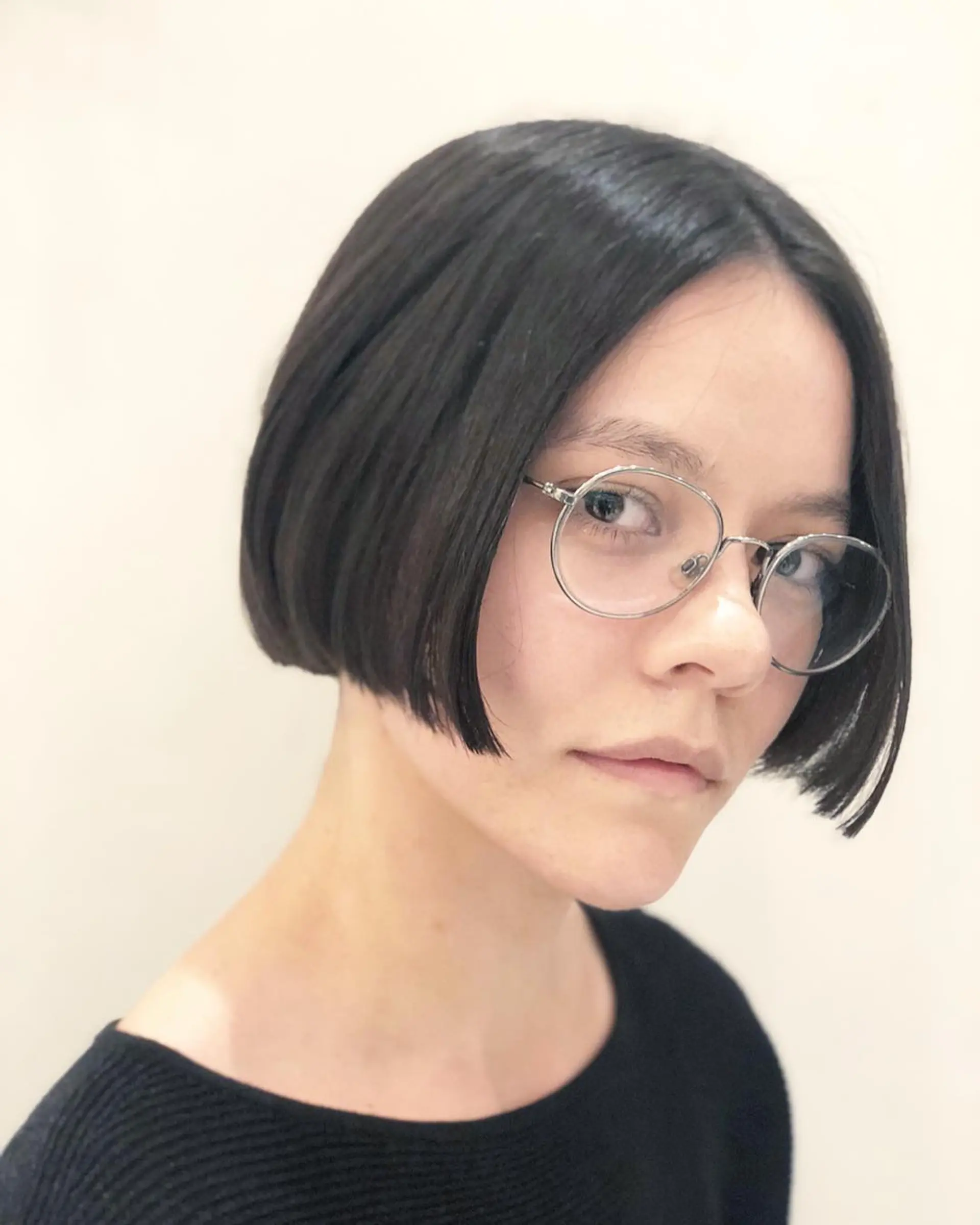 A short, sleek bob with a glossy finish and precision cut, framing the face symmetrically and aligning elegantly with eyewear. 1