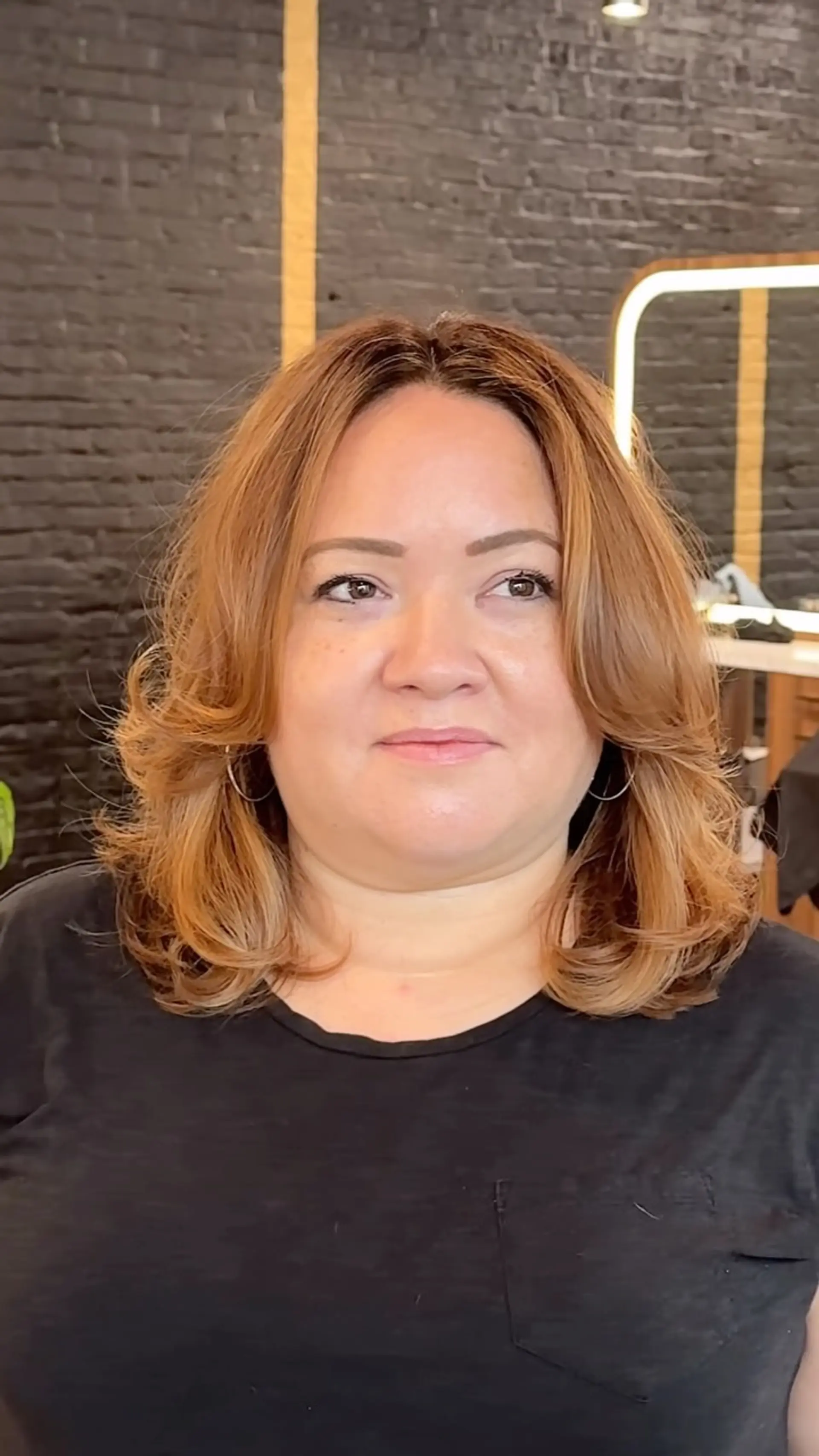 A medium-length layered cut styled with soft, flipped-out ends, curtain bangs, and dimensional warm brunette color. 1