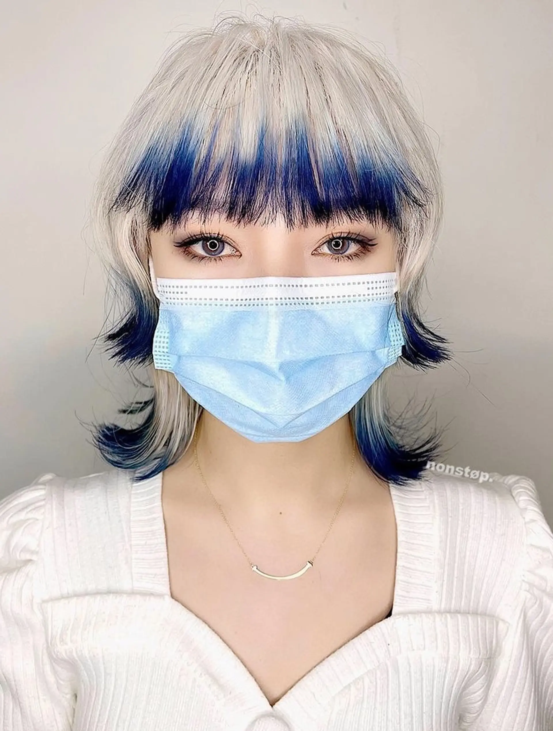 Medium-length hairstyle with a two-tone color of platinum blonde and deep blue, featuring layered cuts, feathered ends, and an edgy fringe. 1