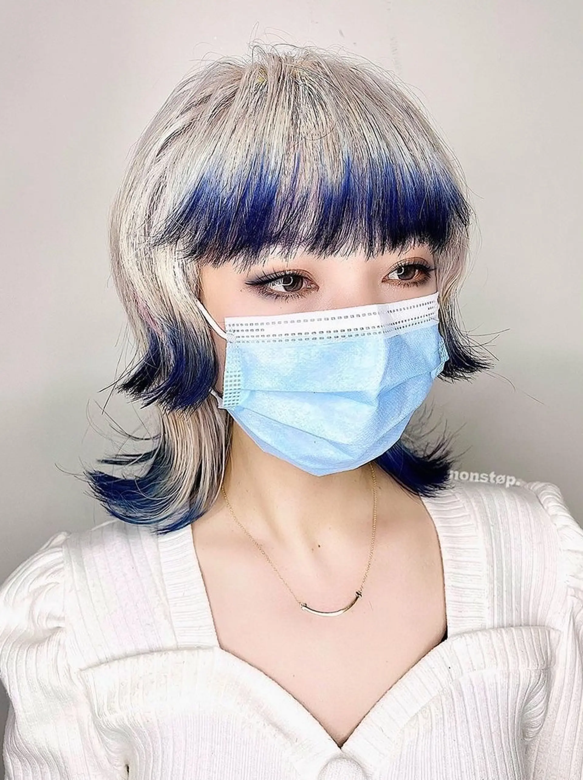 Medium-length hairstyle with a two-tone color of platinum blonde and deep blue, featuring layered cuts, feathered ends, and an edgy fringe. 2