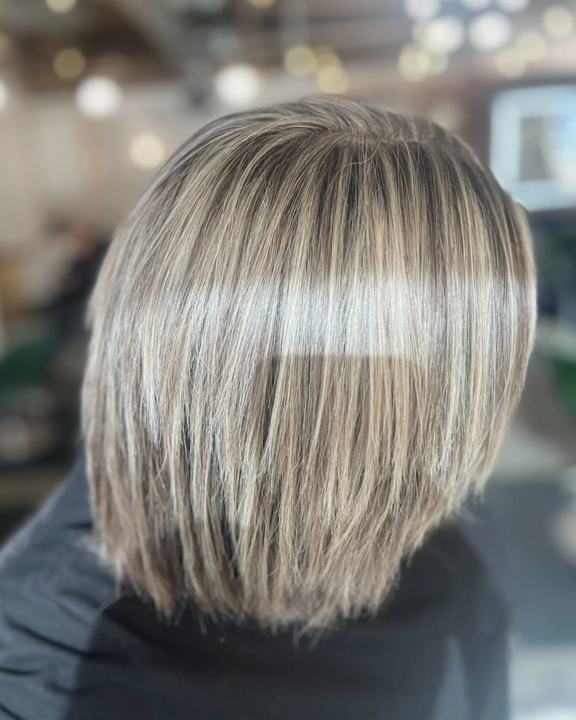 A textured short bob haircut featuring finely blended icy blonde highlights over an ash brown base. 1