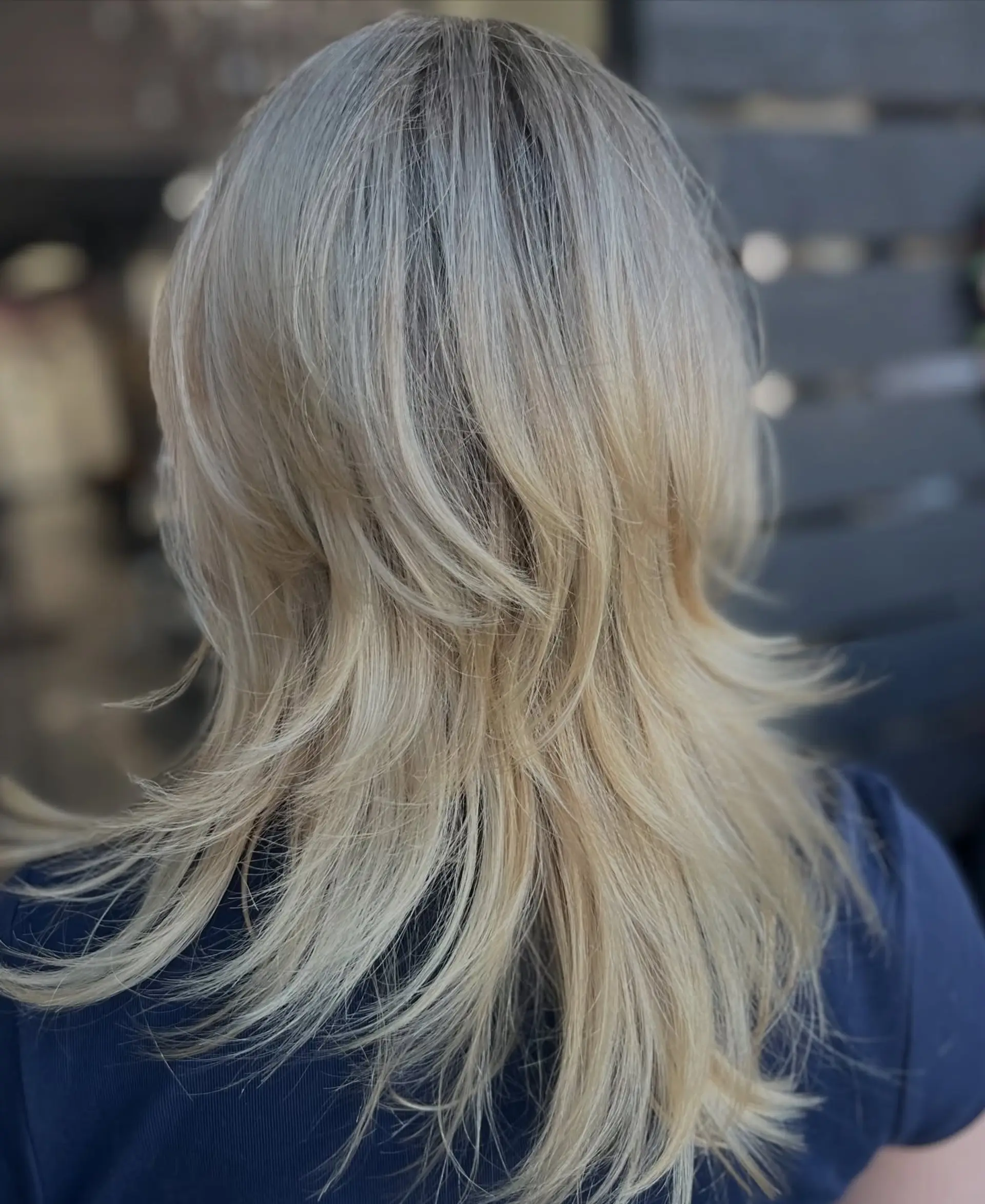 A medium-length feathered shag haircut featuring textured, cascading layers styled with flipped-out ends in a cool light blonde shade. 1