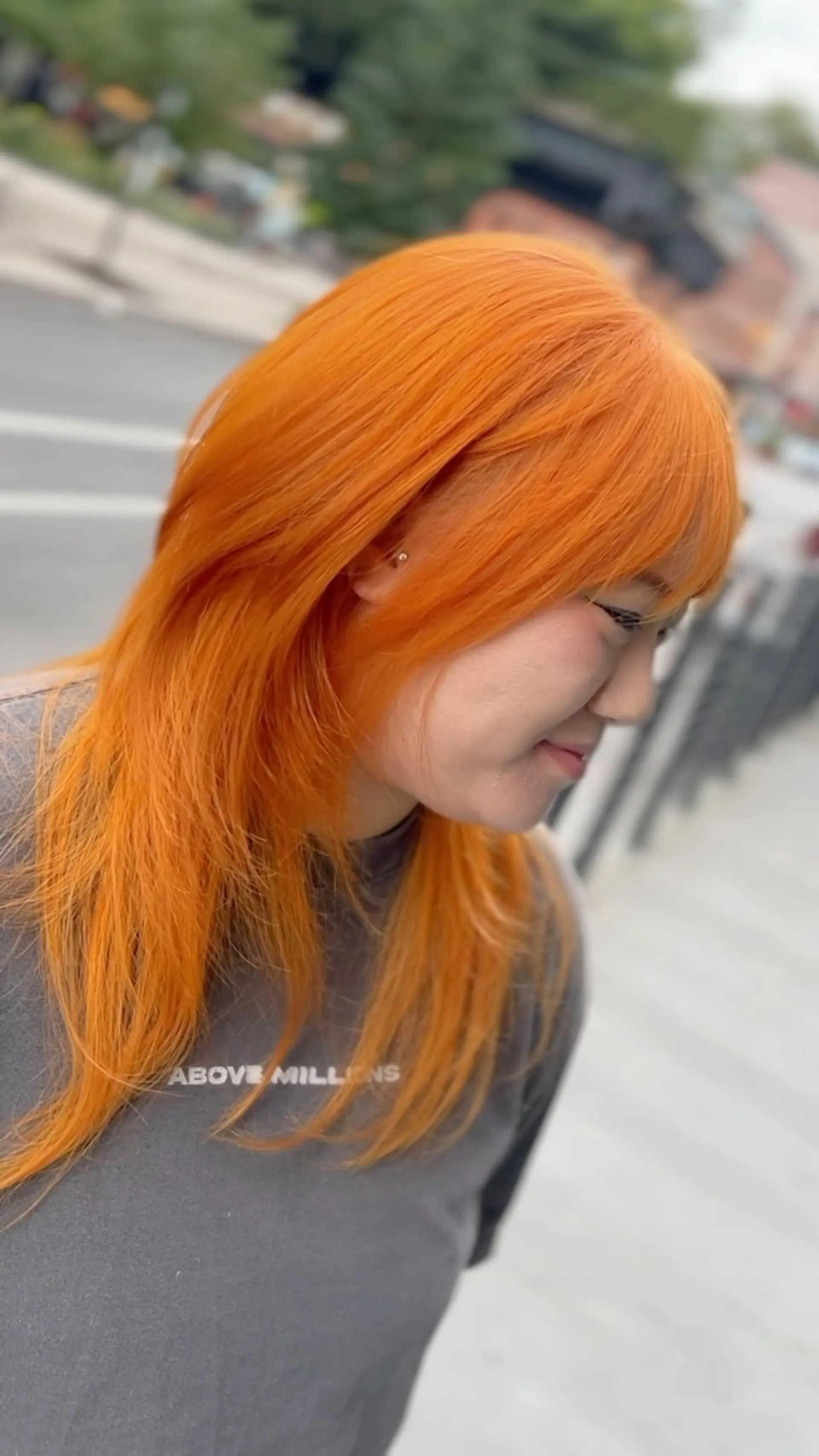 A vivid neon orange medium-length haircut featuring feathered layers and soft brow-skimming bangs. 1