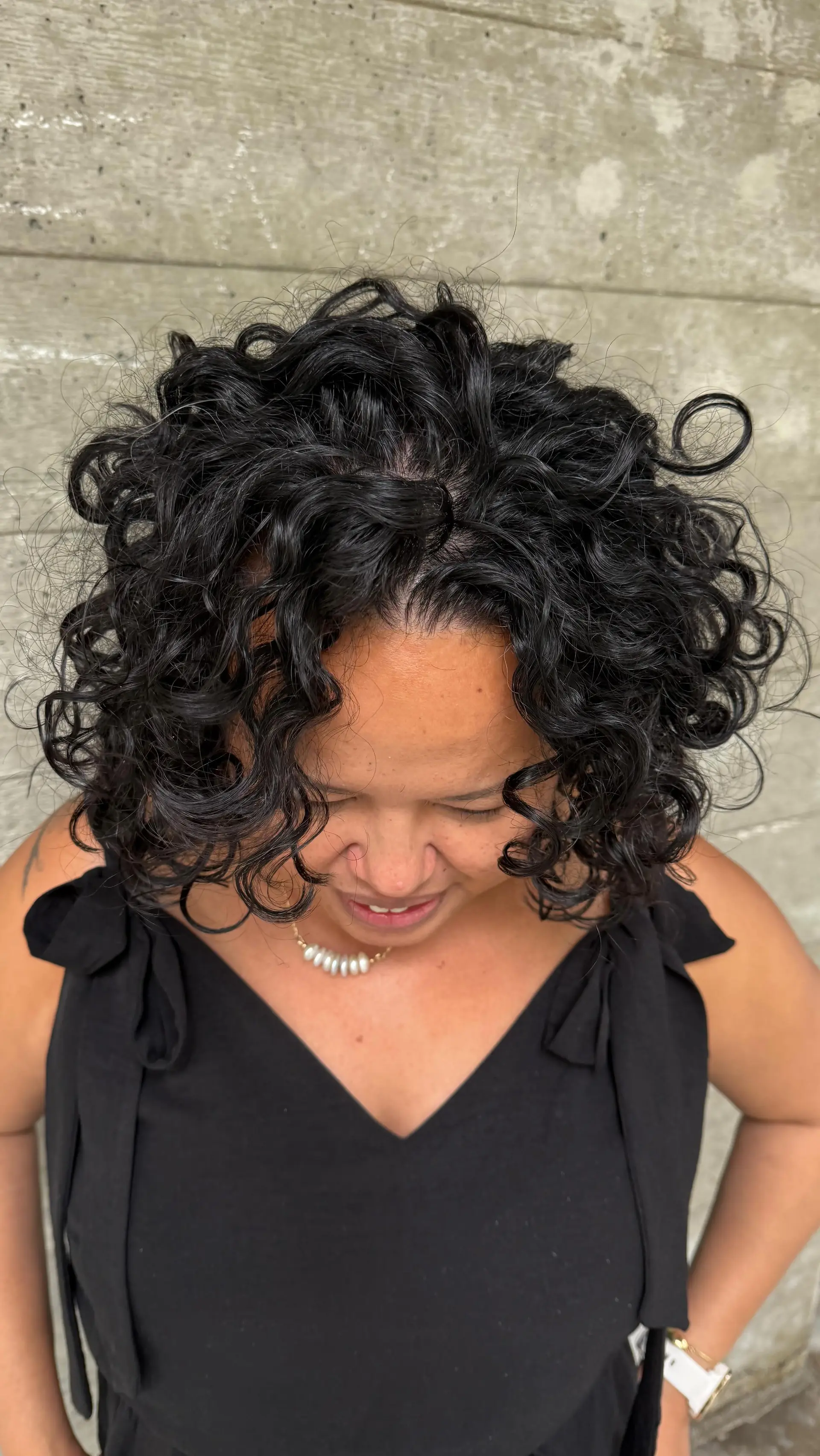 A short, voluminous rounded cut featuring beautifully defined, bouncy natural black curls framing the face. 1