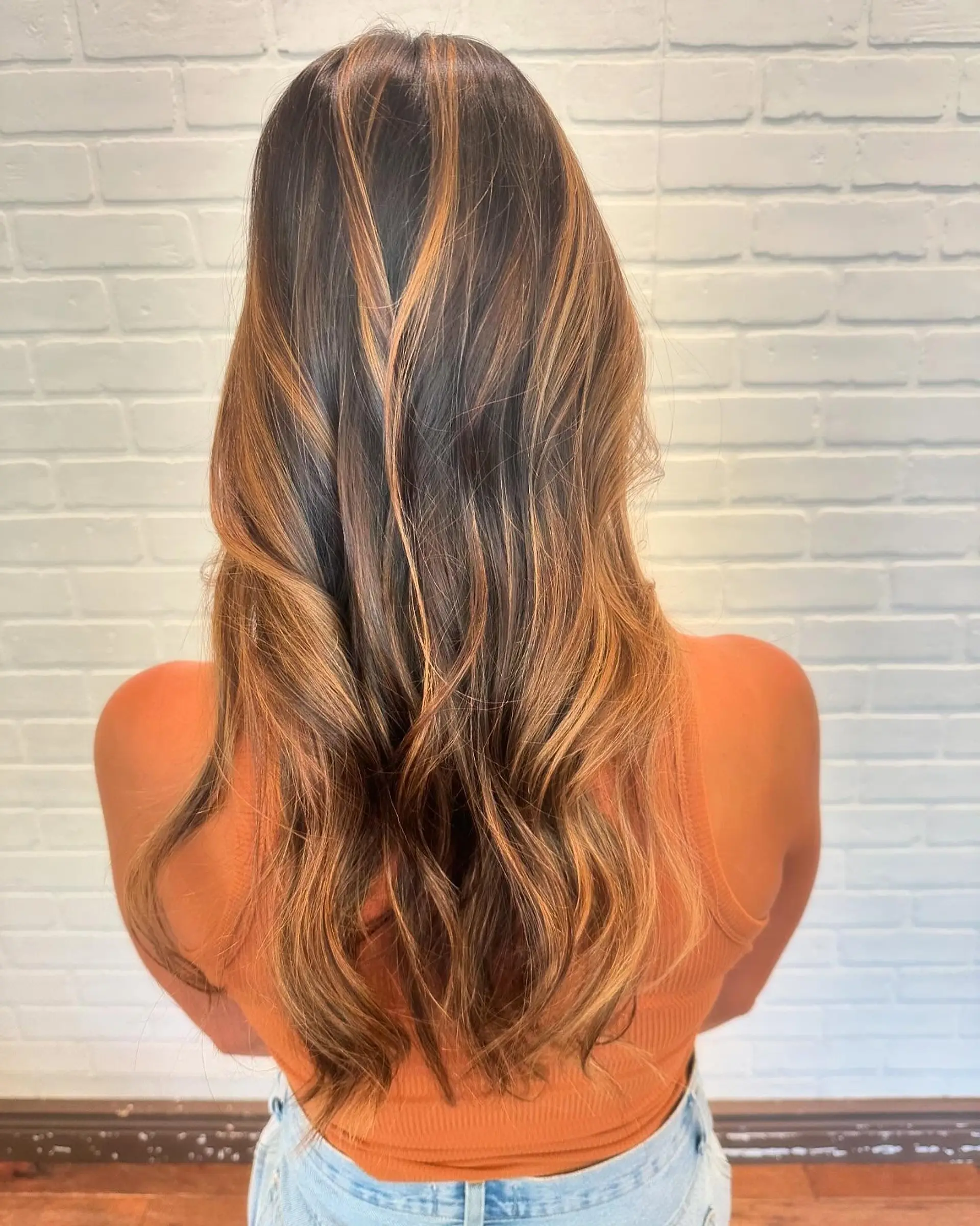 Long dark brown hair styled in soft waves with warm caramel and golden ombré highlights through the mid-lengths and ends. 1